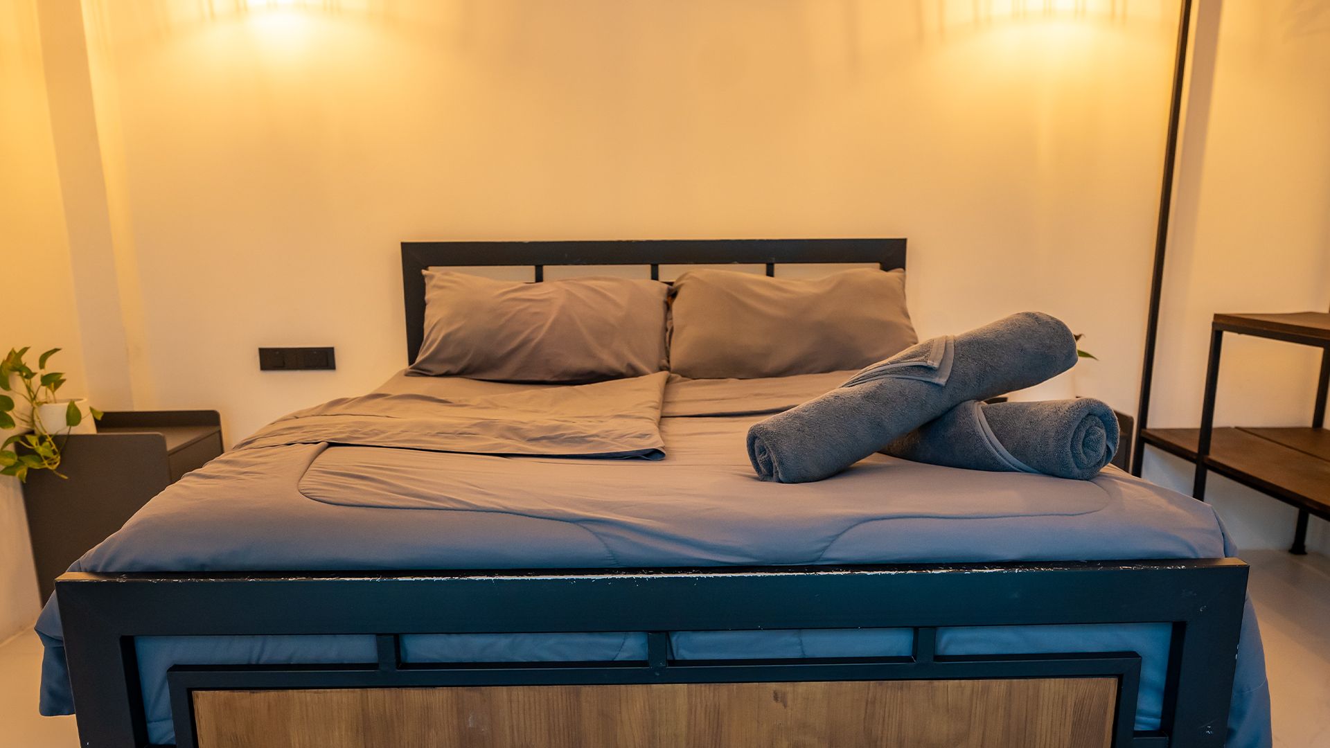 Neatly made bed with gray bedding and crossed denim-clad legs in a softly lit bedroom