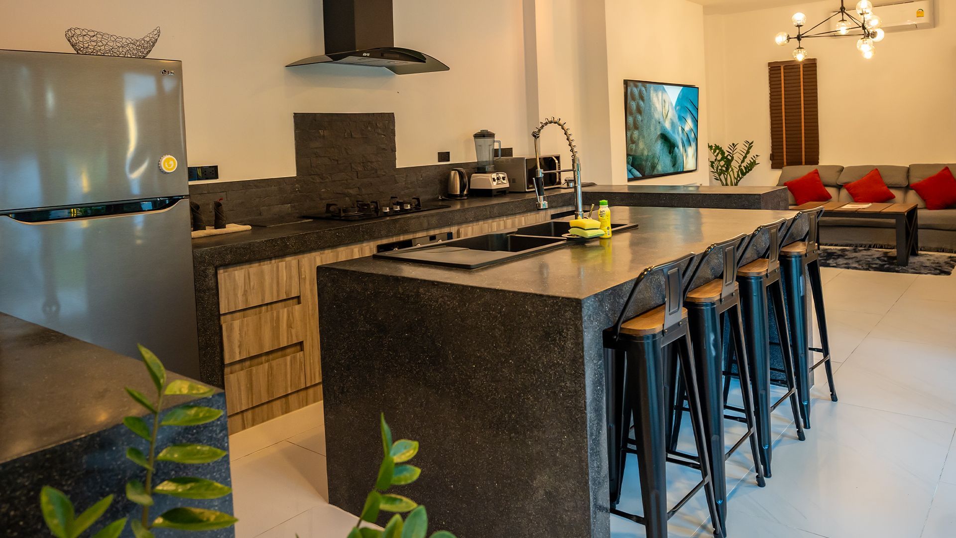 Modern kitchen with dark island, bar stools, stainless fridge, and a bright adjoining living area