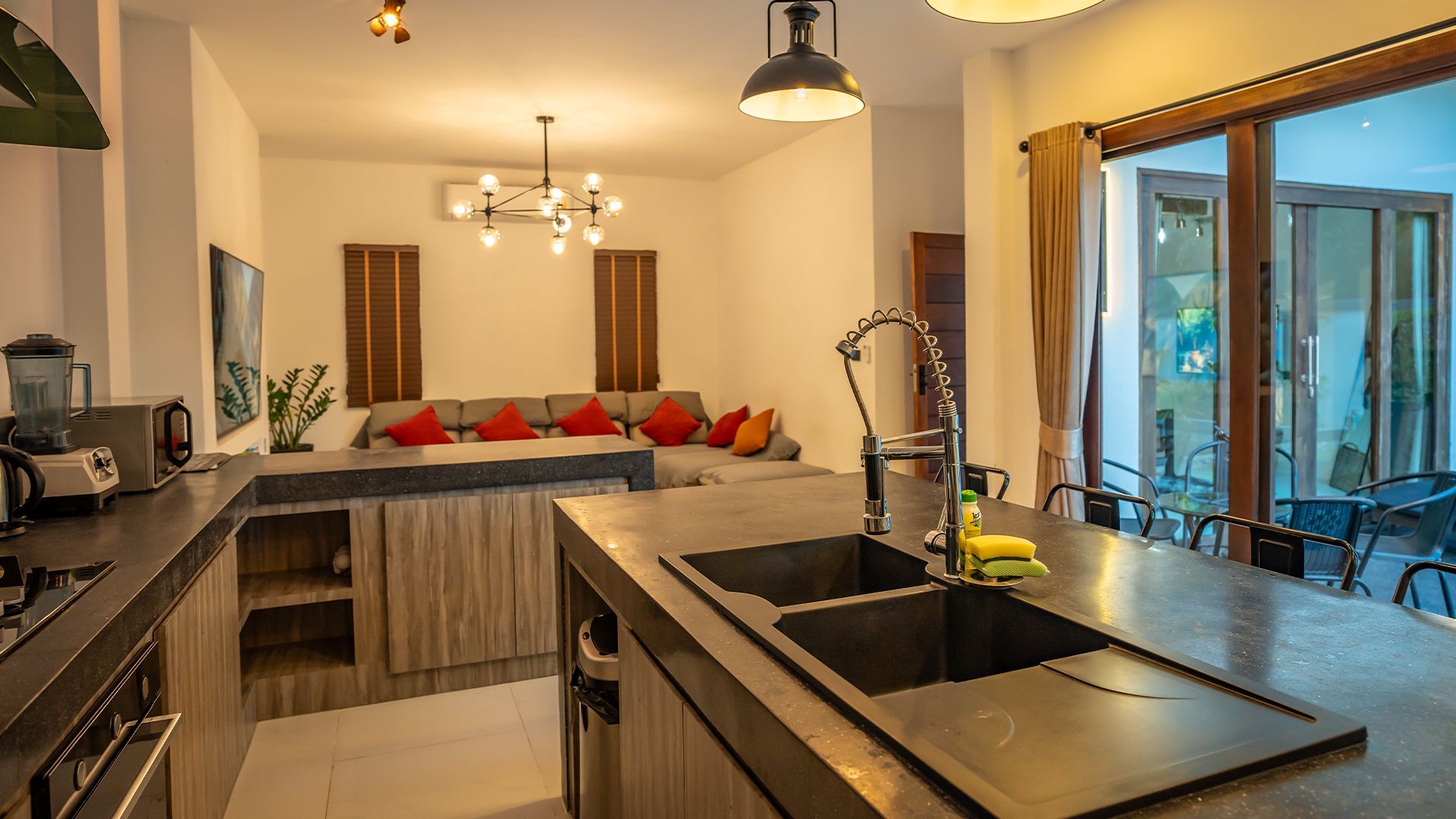 Modern kitchen with dark counters, island sink, and adjacent dining nook with red cushions and glass doors
