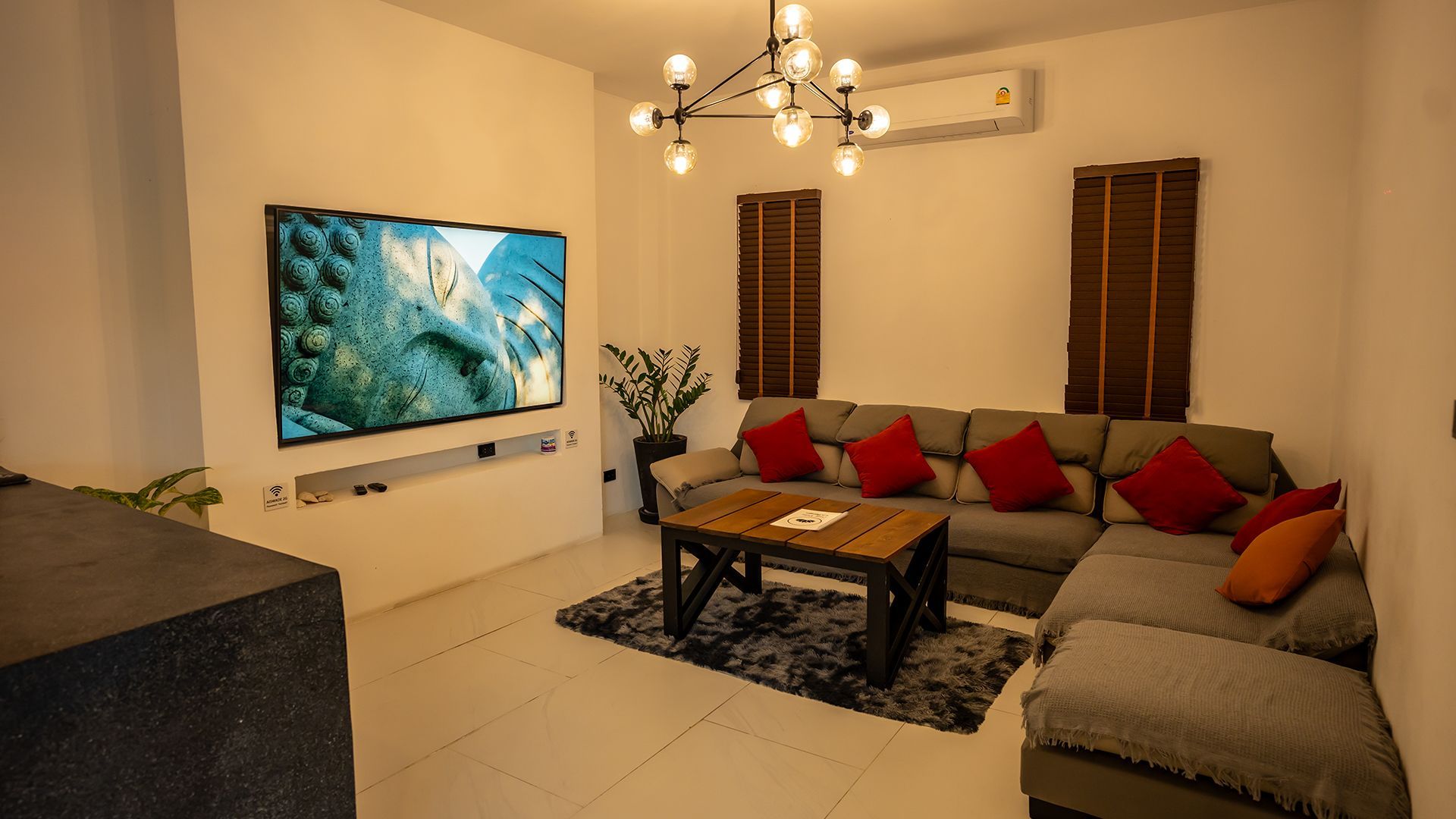 Modern living room with wall-mounted TV, sectional sofa, coffee table, and chandelier on warm beige walls.