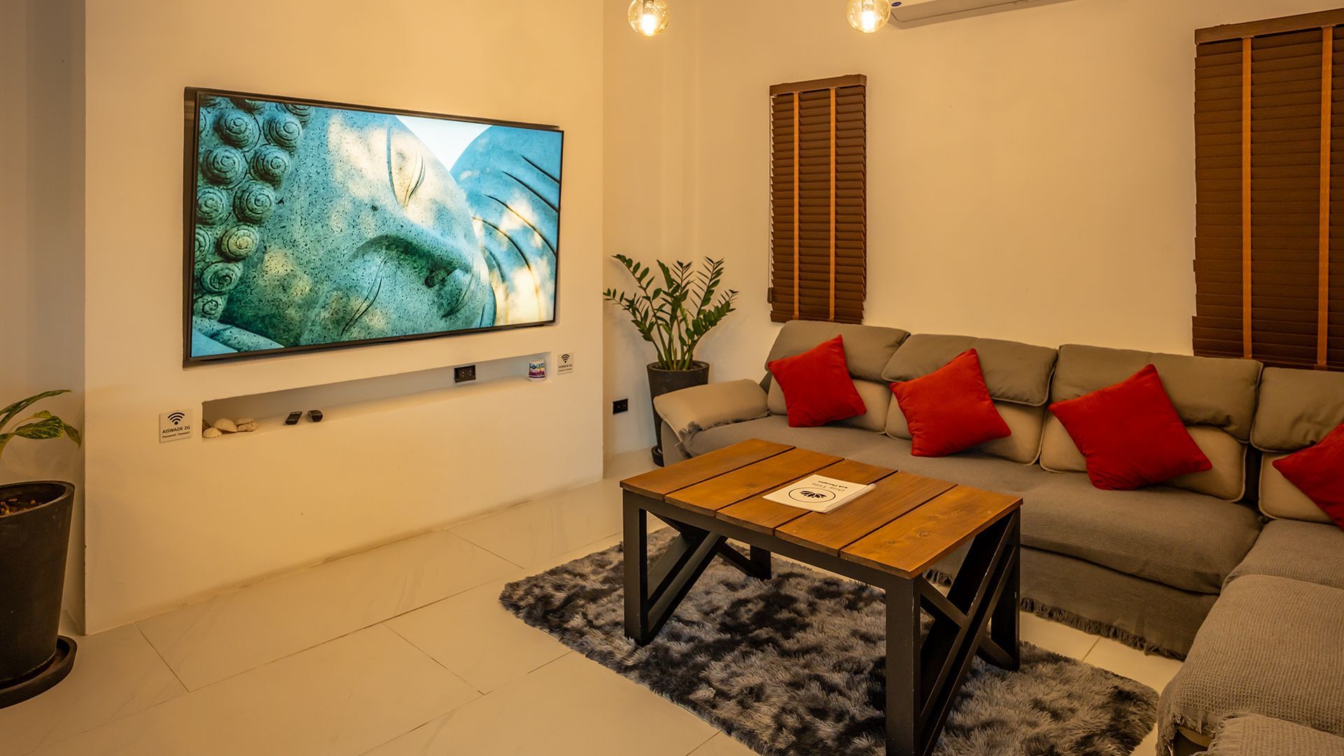 Modern living room with wall-mounted TV, beige sofa with red cushions, and wooden coffee table