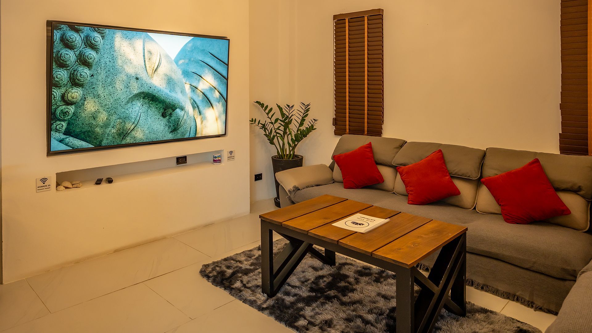 Modern living room with wall-mounted TV, gray sofa with red pillows, coffee table, and shag rug