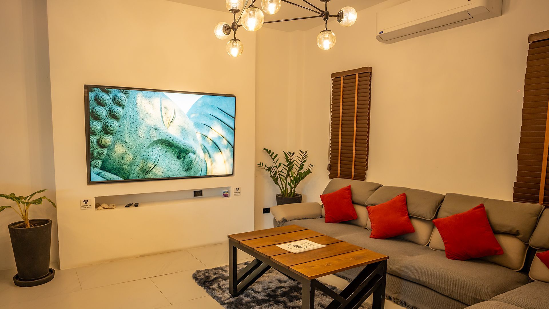 Modern living room with gray sofa, red pillows, wall-mounted TV, coffee table, and warm lighting