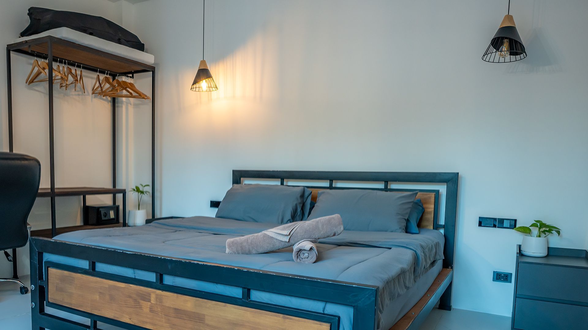 Modern bedroom with a blue-gray bed, hanging lights, clothing rack, and minimalist decor