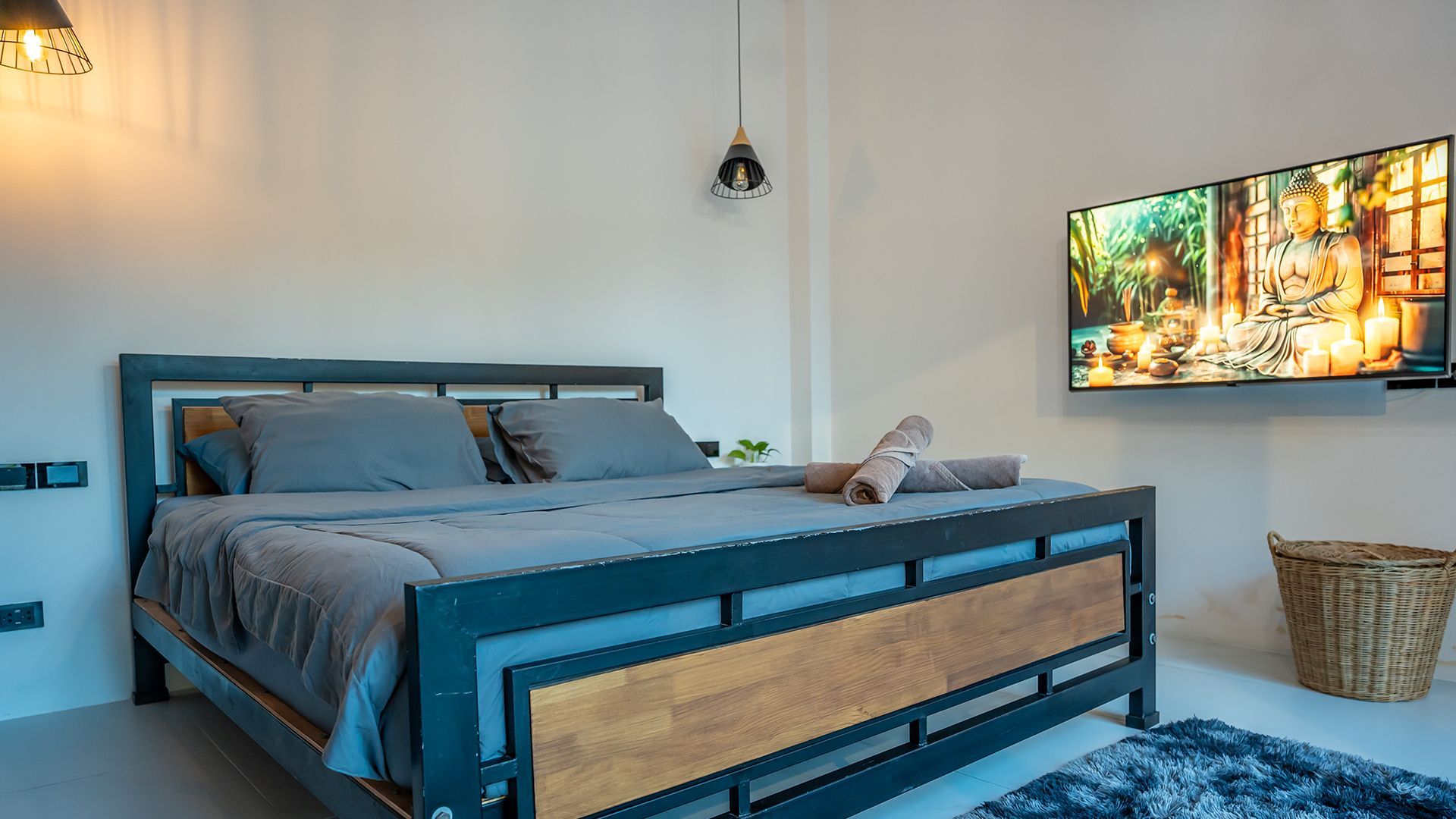Modern bedroom with a blue-gray bed, wall-mounted TV, and wicker basket on a white wall.
