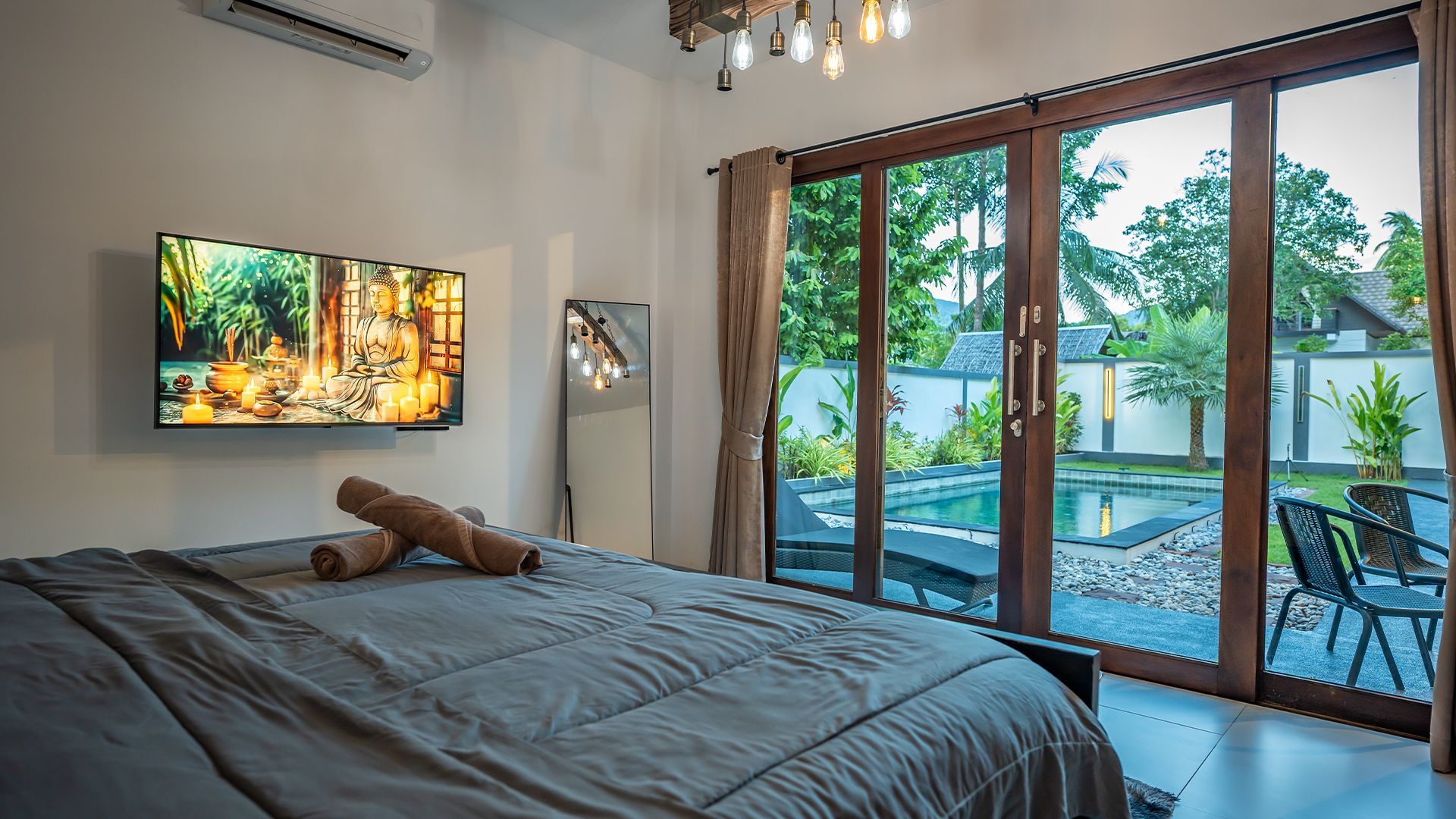 Modern bedroom with a bed, wall TV, and sliding glass doors opening to a pool patio and greenery