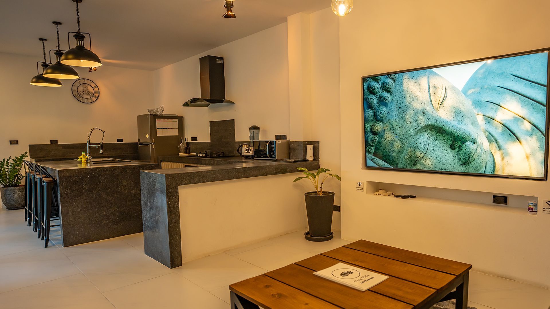 Modern open-plan kitchen and living room with island, wall-mounted TV, and wooden coffee table.