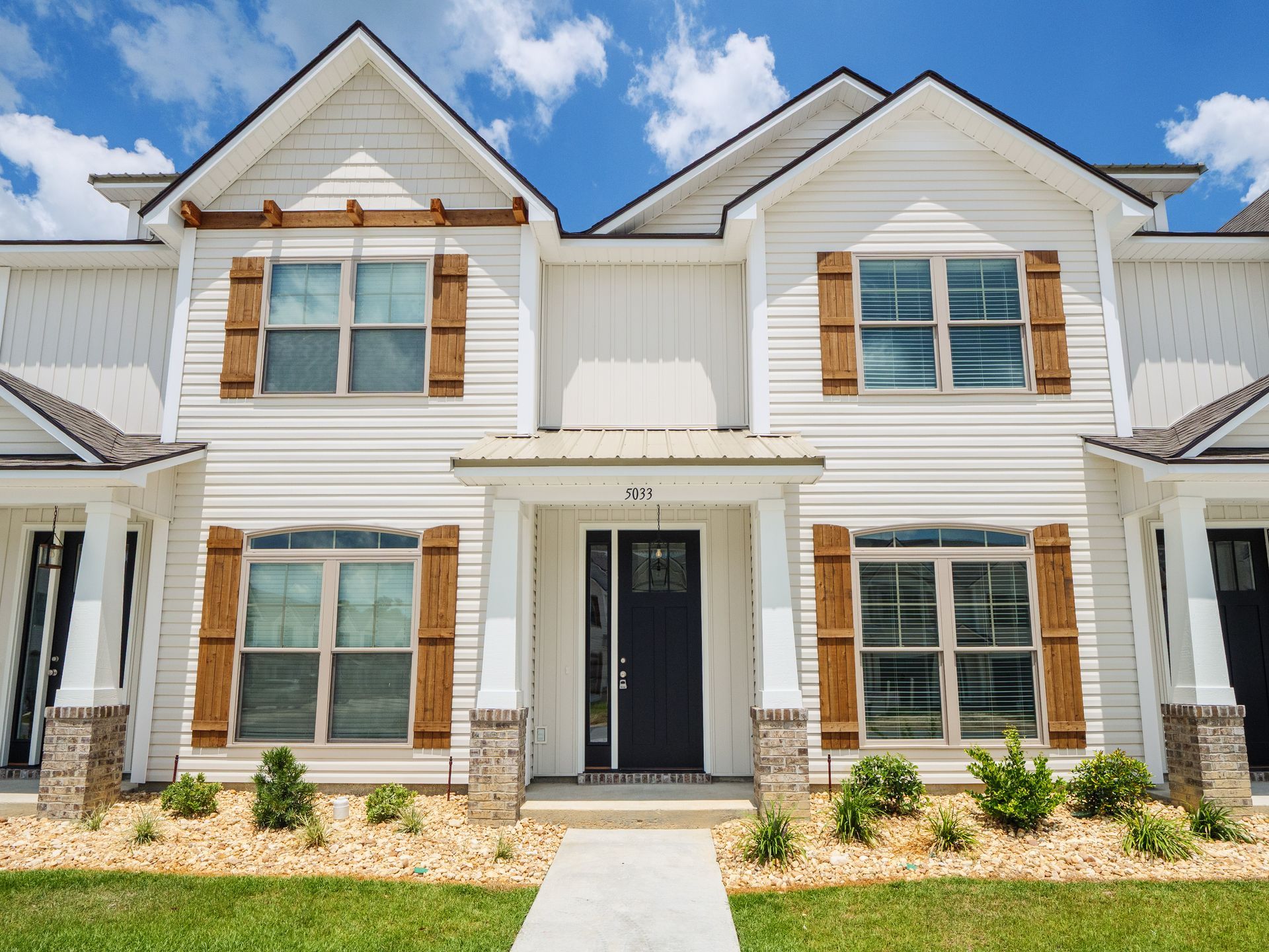 Row of modern white townhouses with tan brick accents and wood shutters under a partly cloudy sky