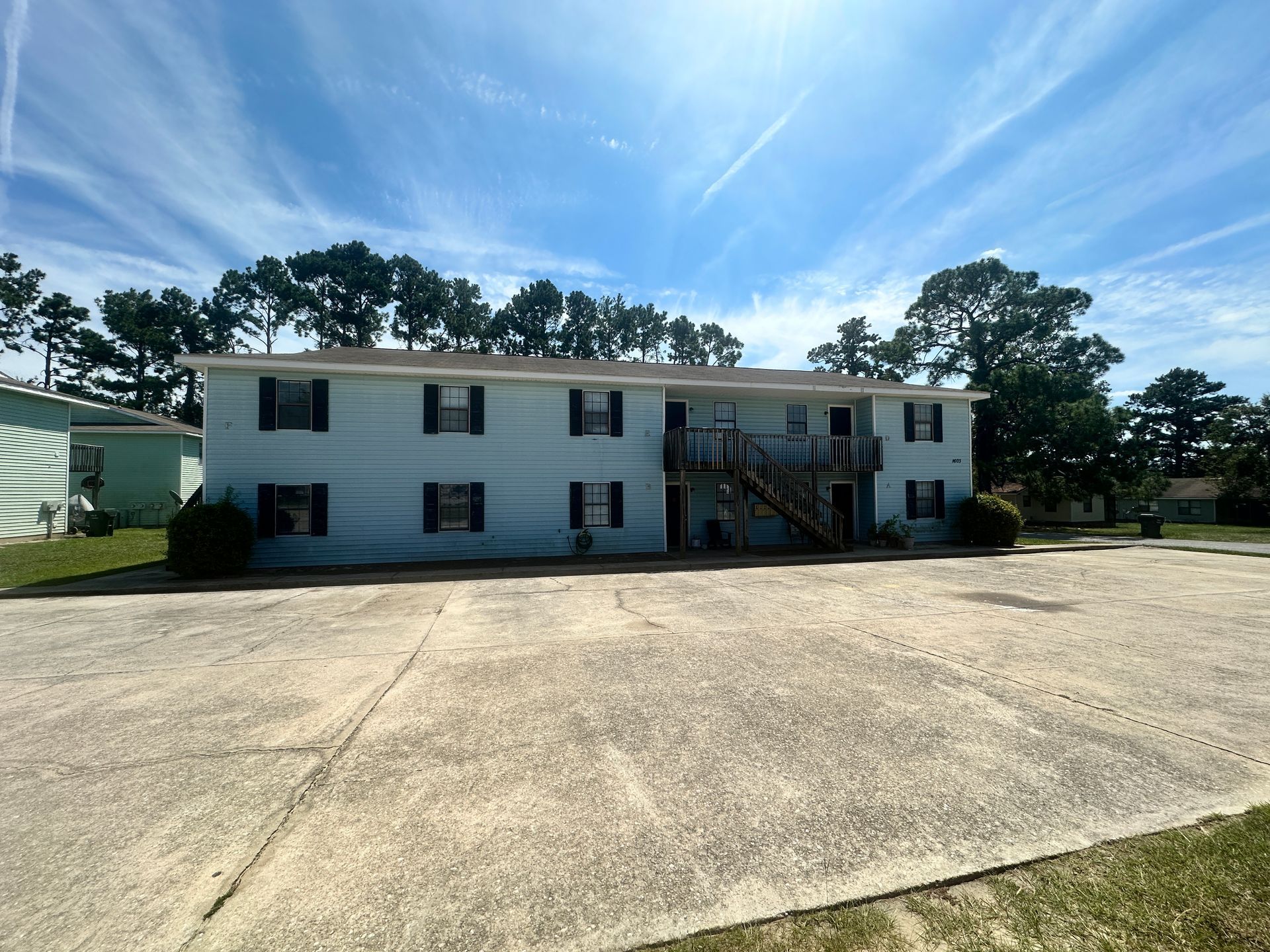 Two-story white apartment building with exterior stairs and a large paved lot under a blue sky
