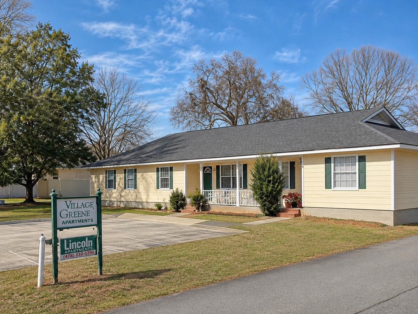 Single-story beige house with a front porch, lawn, and a sign by the road