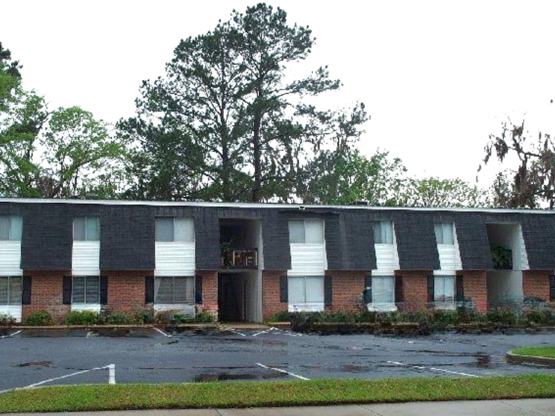 Two-story brick apartment building with white awnings, a central entrance, and wet pavement in front