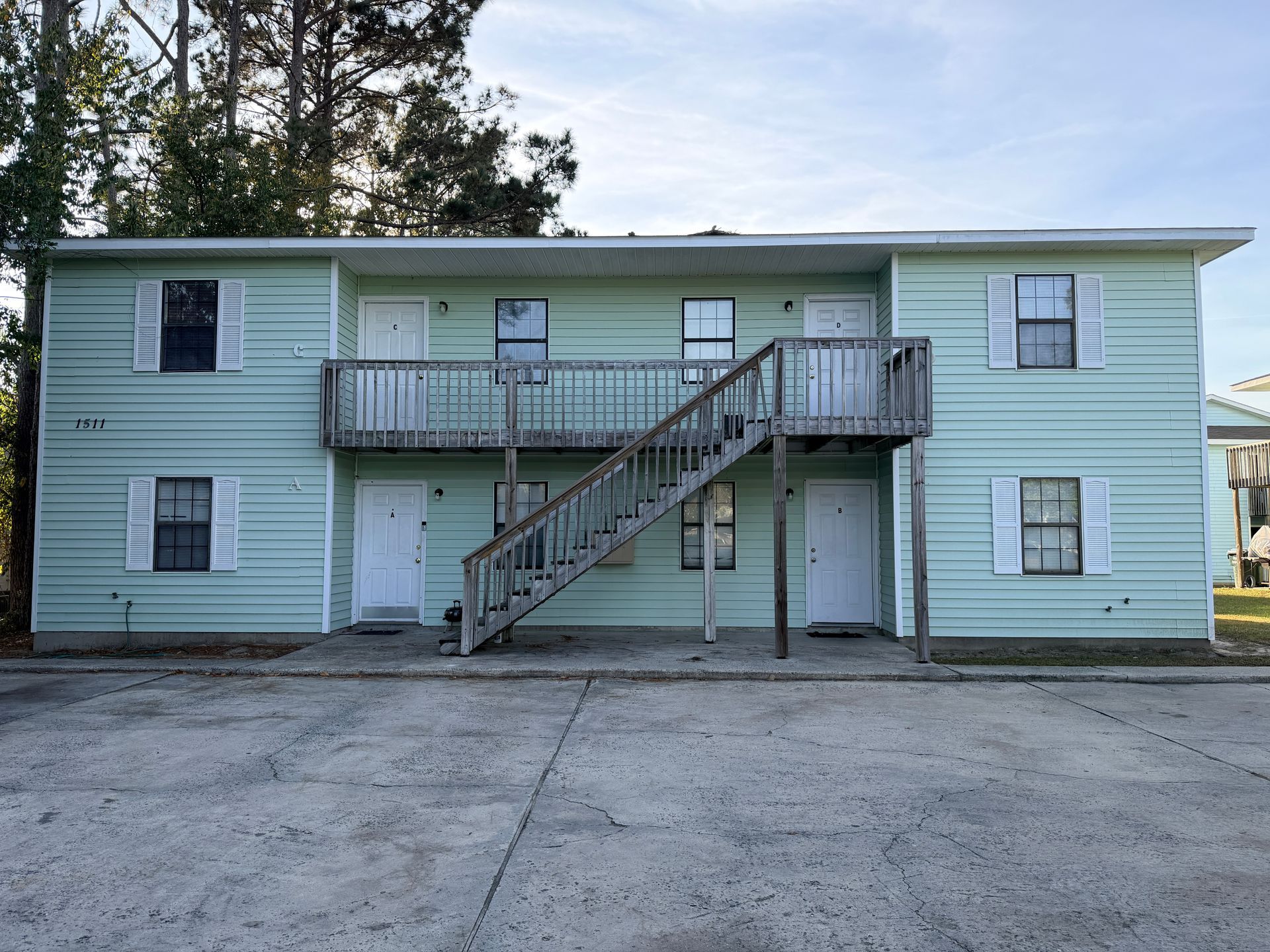 Two-story white apartment building with black shutters and exterior stairs under a sunny sky