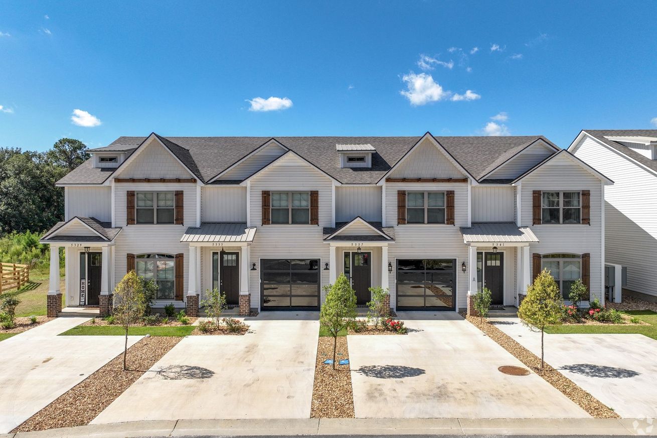 Row of modern white townhomes with garages and driveways under a blue sky