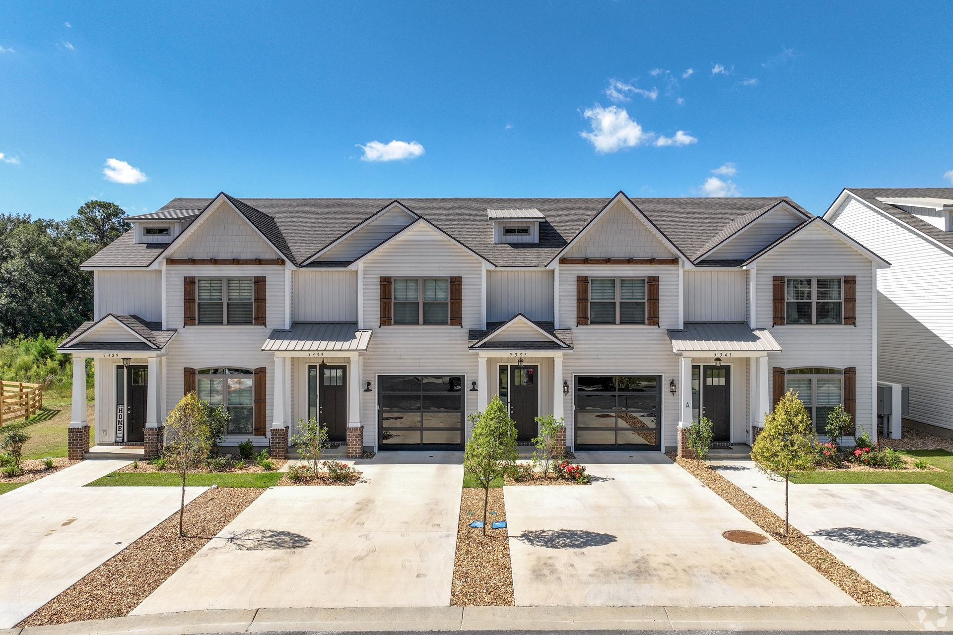 Row of modern white townhomes with garages and driveways under a blue sky