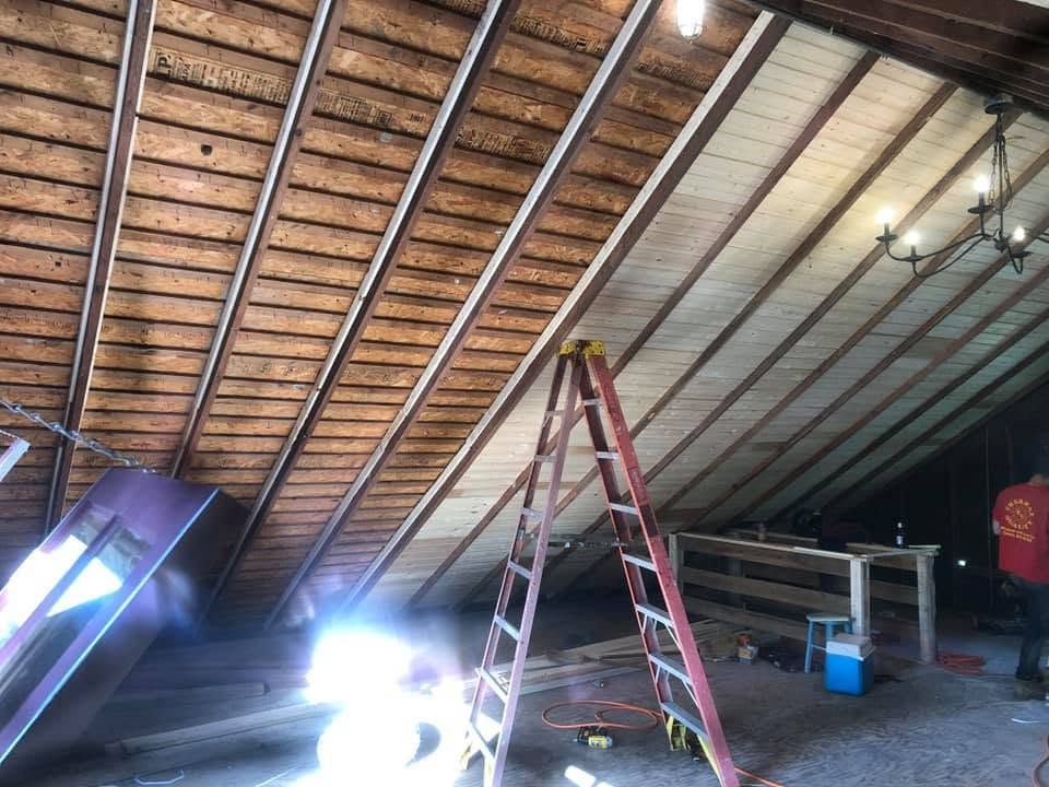Interior with exposed roof beams, ladder, and workbench in an unfinished garage or attic area. Interior with exposed roof beams, ladder, and workbench in an unfinished garage or attic area.