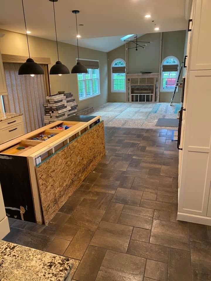 Empty modern kitchen with island, dark tile floor, pendant lights, and a living area with large windows beyond Empty modern kitchen with island, dark tile floor, pendant lights, and a living area with large windows beyond