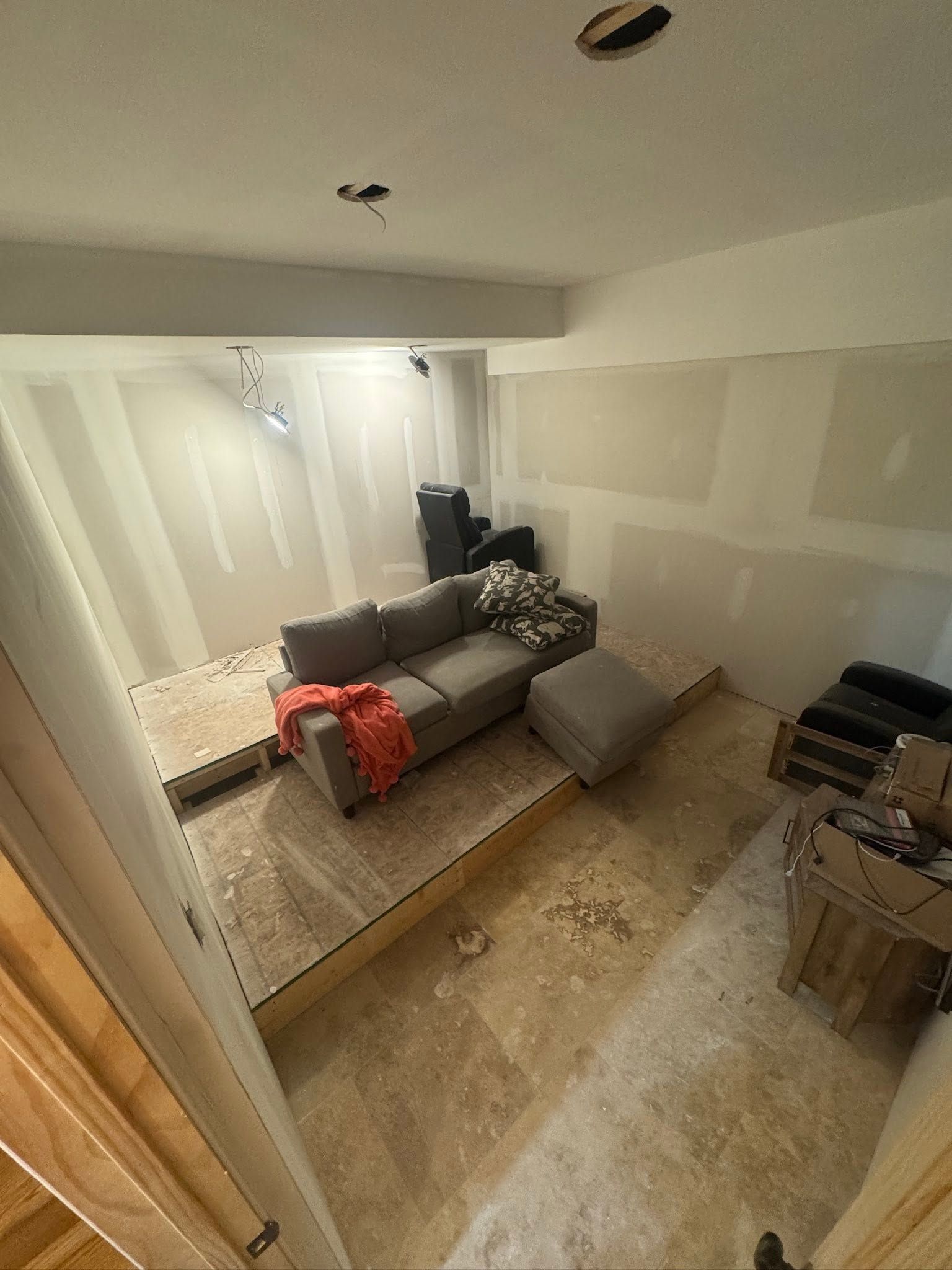 Partially renovated room with taped drywall, a couch, boxes, and construction materials. Partially renovated room with taped drywall, a couch, boxes, and construction materials.