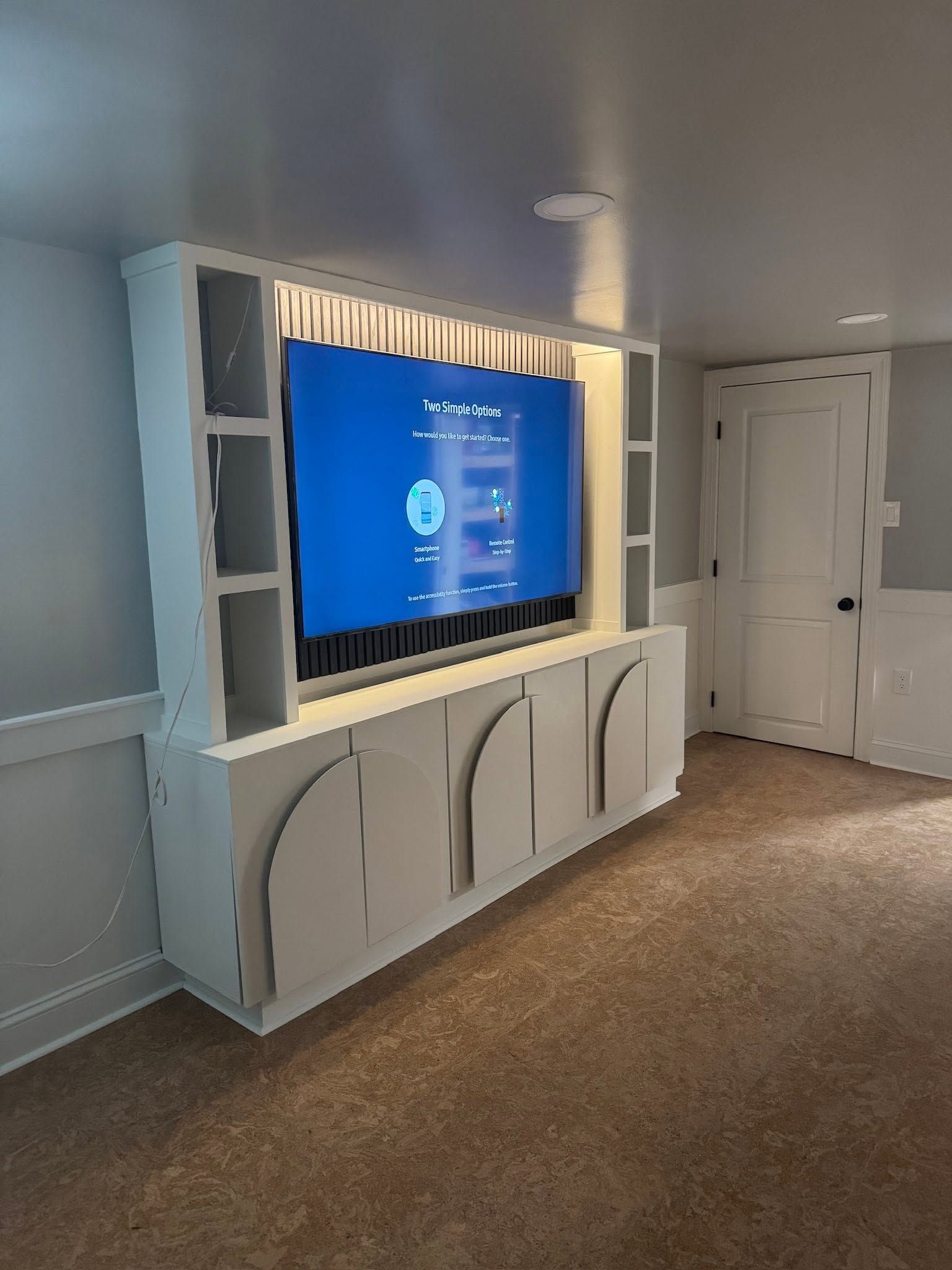 Built-in TV and cabinetry in a carpeted room with a hallway and closed door. Built-in TV and cabinetry in a carpeted room with a hallway and closed door.