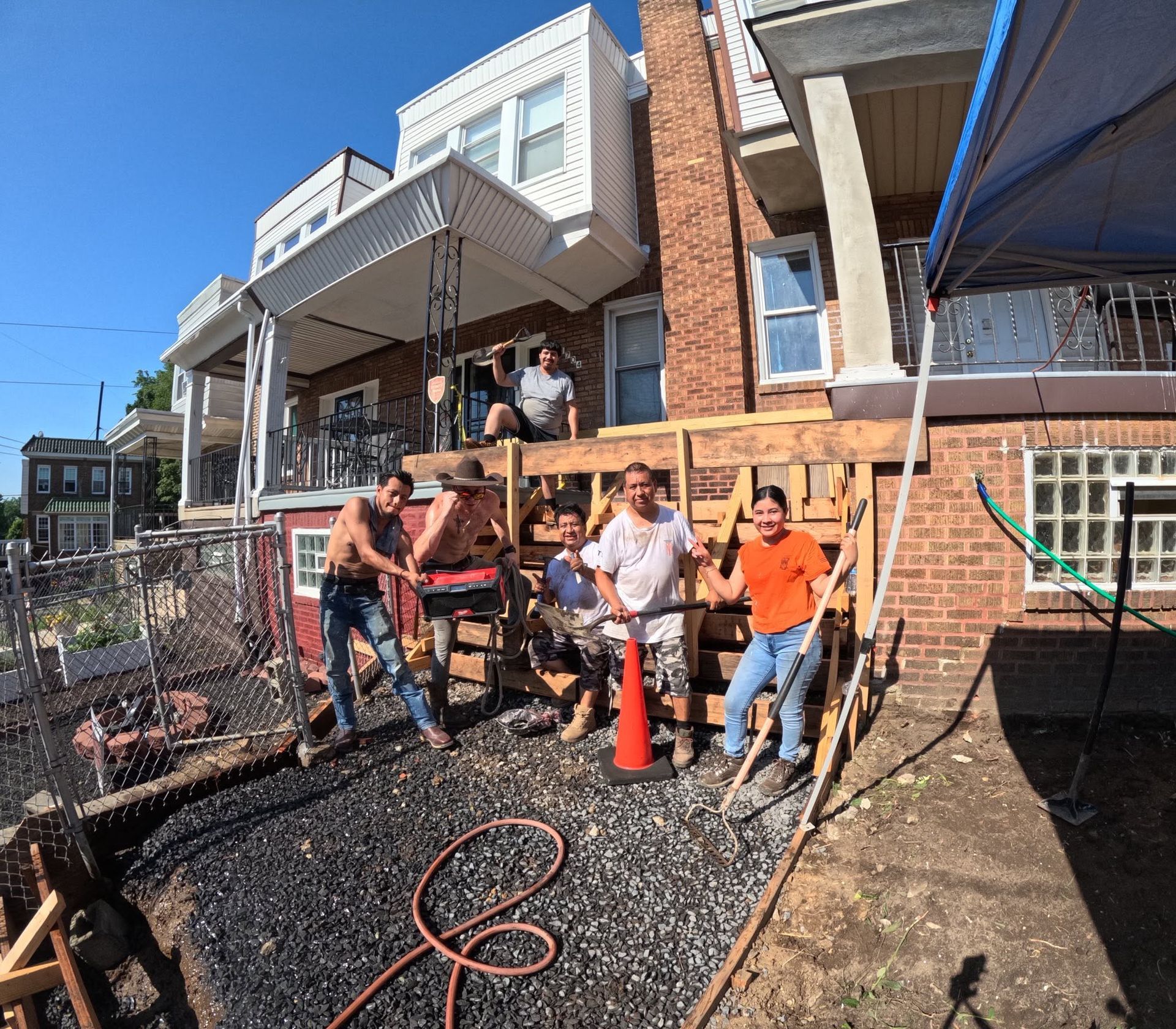 Workers installing a retaining wall on a brick townhouse patio, with tools, gravel, and orange safety cone. Workers installing a retaining wall on a brick townhouse patio, with tools, gravel, and orange safety cone.