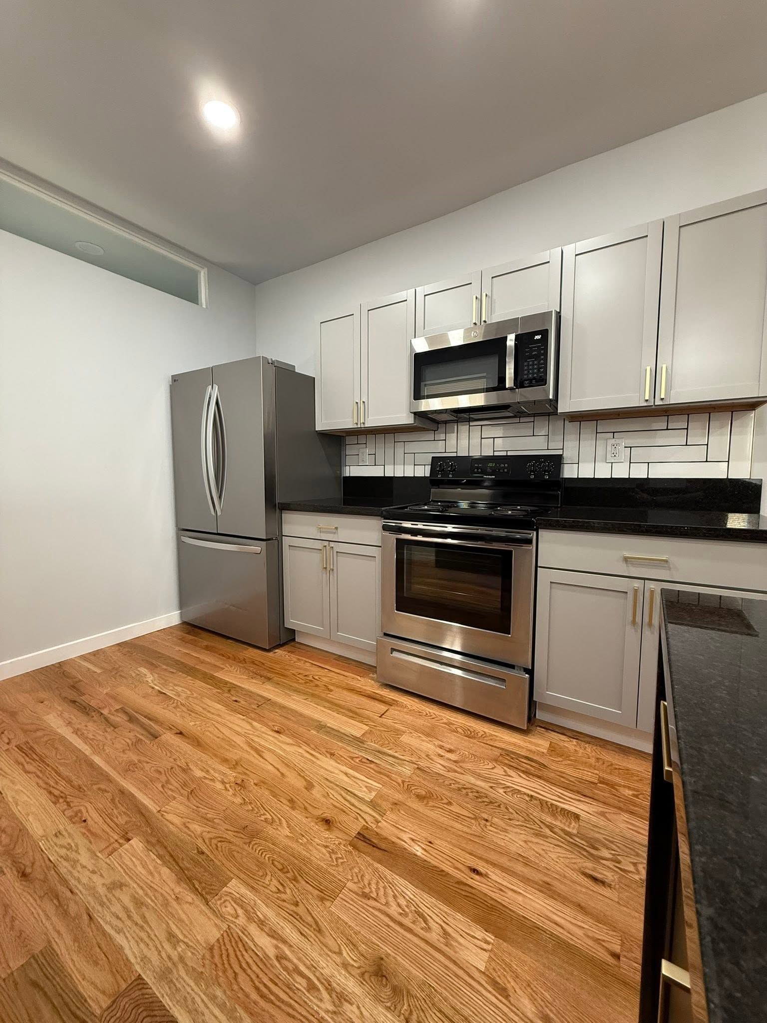 Modern kitchen with stainless steel appliances, white cabinets, black countertops, and wood flooring. Modern kitchen with stainless steel appliances, white cabinets, black countertops, and wood flooring.