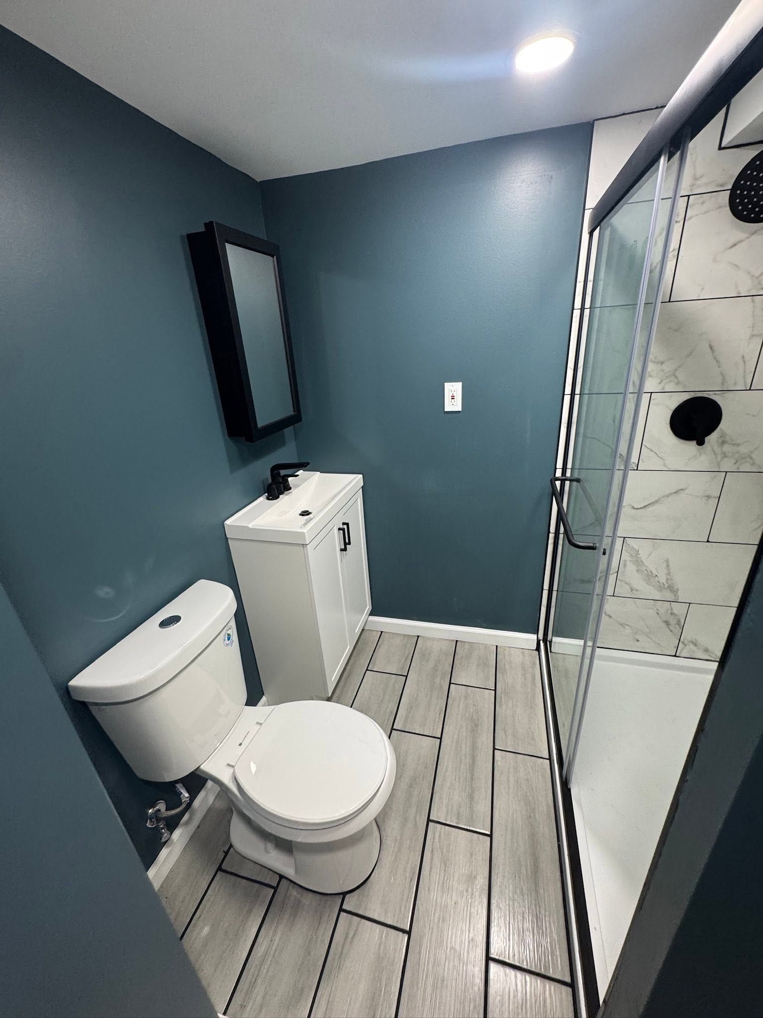 Small bathroom with toilet, sink, shower, gray walls, and tiled floor. Small bathroom with toilet, sink, shower, gray walls, and tiled floor.