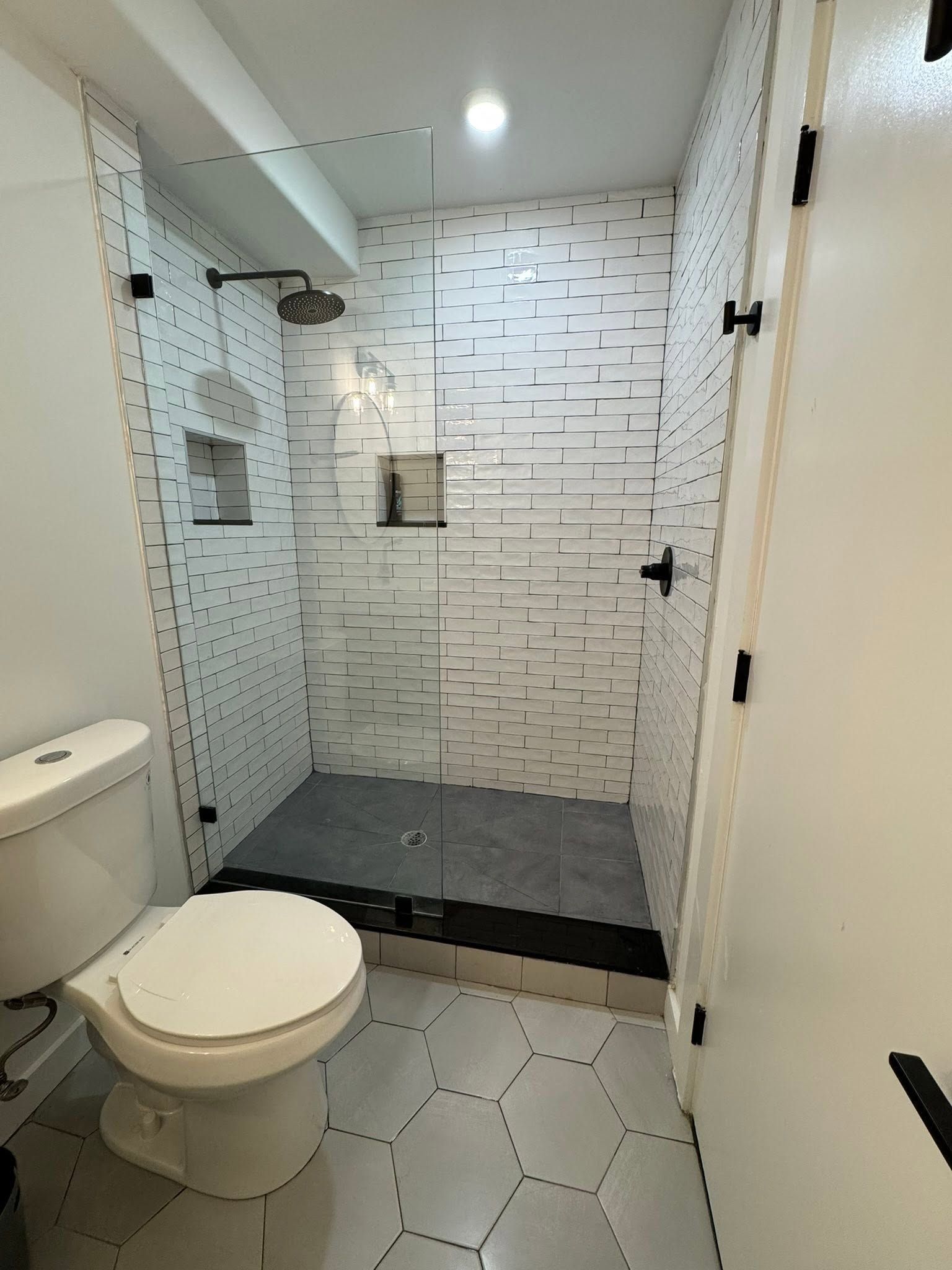Small bathroom with toilet, glass shower, and white tile walls and floor. Small bathroom with toilet, glass shower, and white tile walls and floor.
