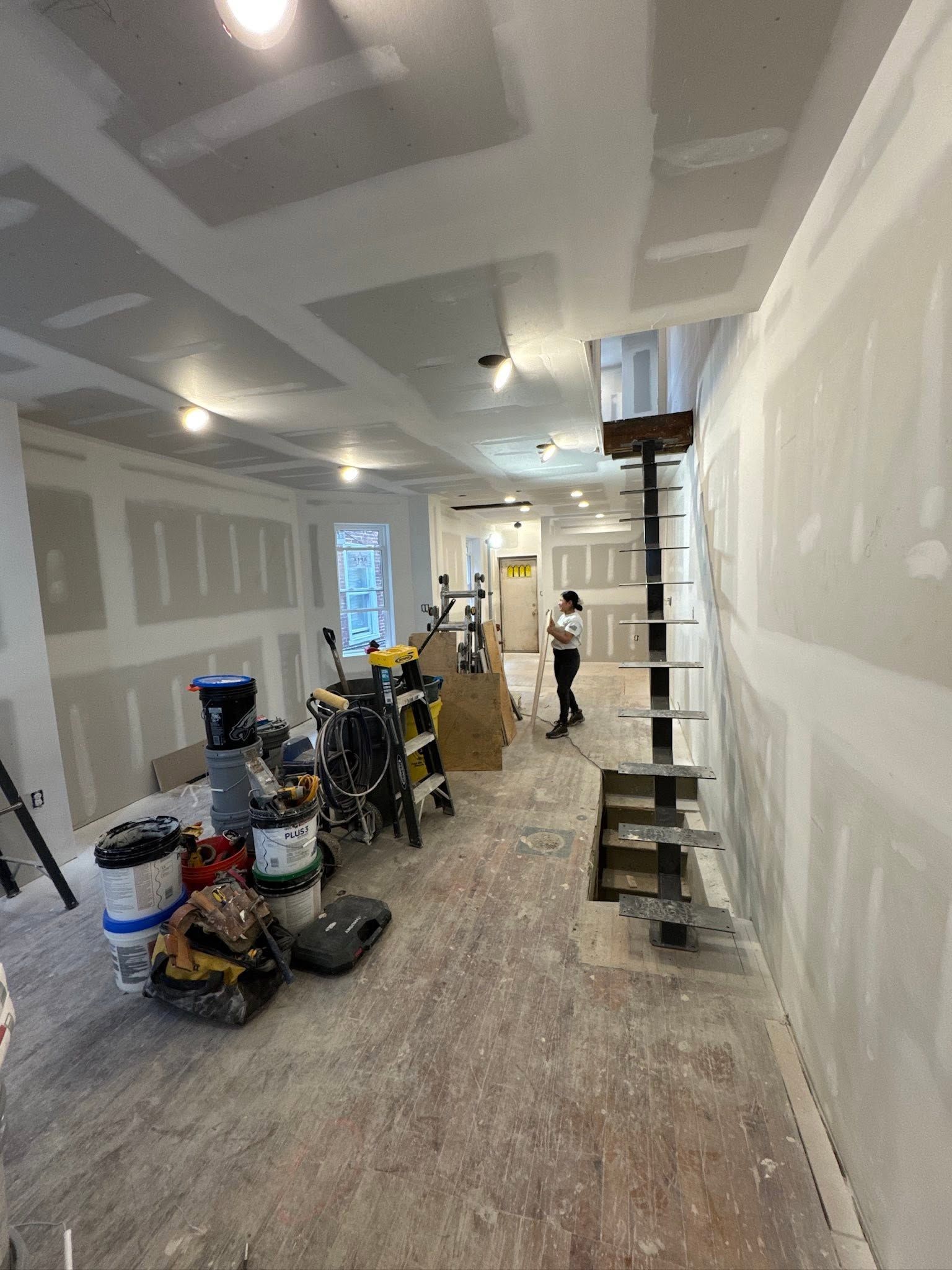 Partially finished room with drywall, ladders, tools, and workers renovating inside. Partially finished room with drywall, ladders, tools, and workers renovating inside.
