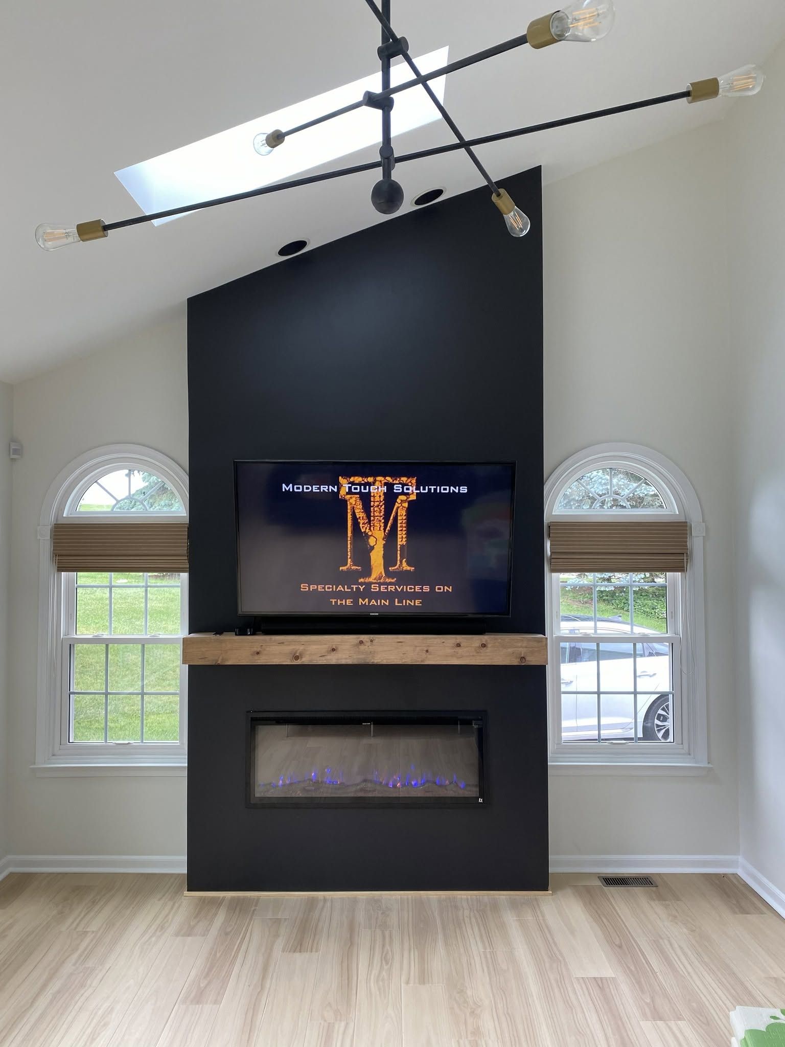 Modern living room with black fireplace wall, mounted TV, and arched windows under a vaulted ceiling