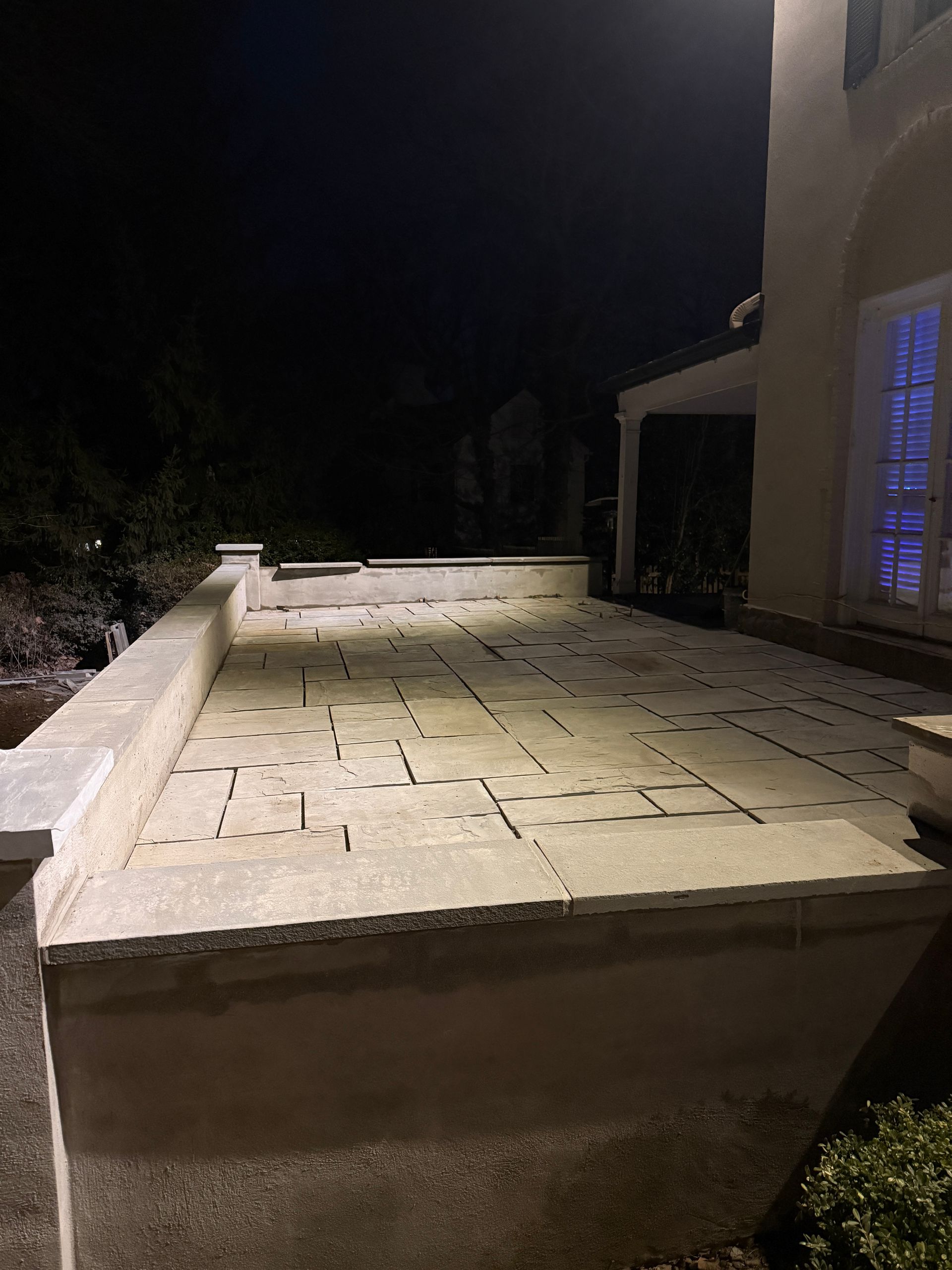 Night view of a flat rooftop terrace beside a building, with stone tiles and low walls.