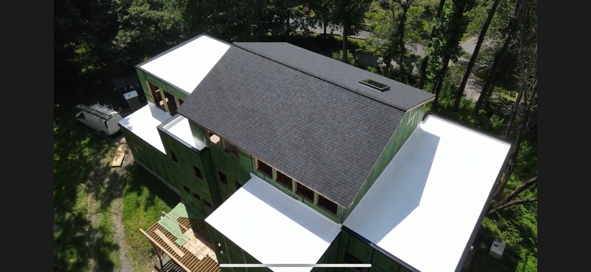 Aerial view of a modern dark-roofed house surrounded by trees and white patio decks