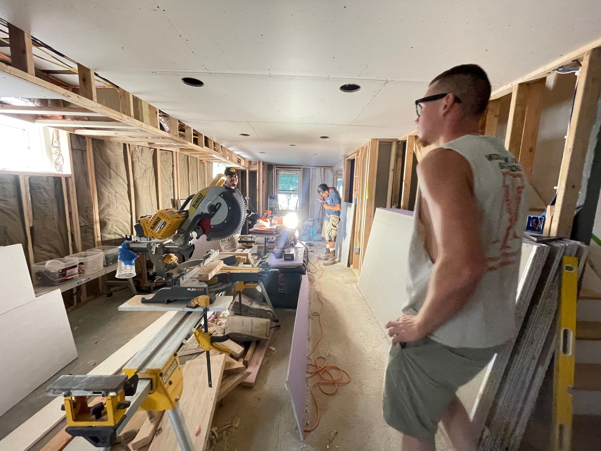 People working inside a house under renovation, with tools and exposed wall framing. People working inside a house under renovation, with tools and exposed wall framing.