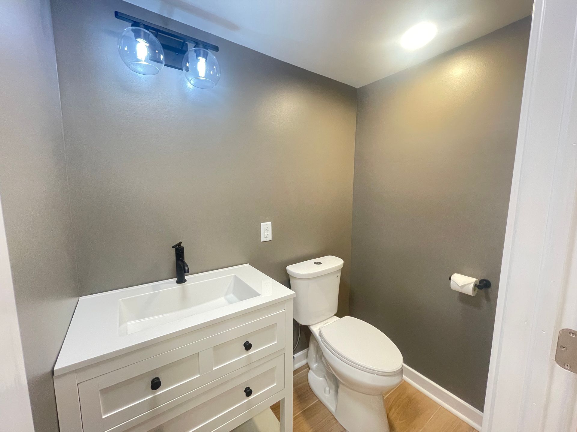 Small bathroom with toilet, sink, shower, gray walls, and tiled floor. Small bathroom with toilet, sink, shower, gray walls, and tiled floor.