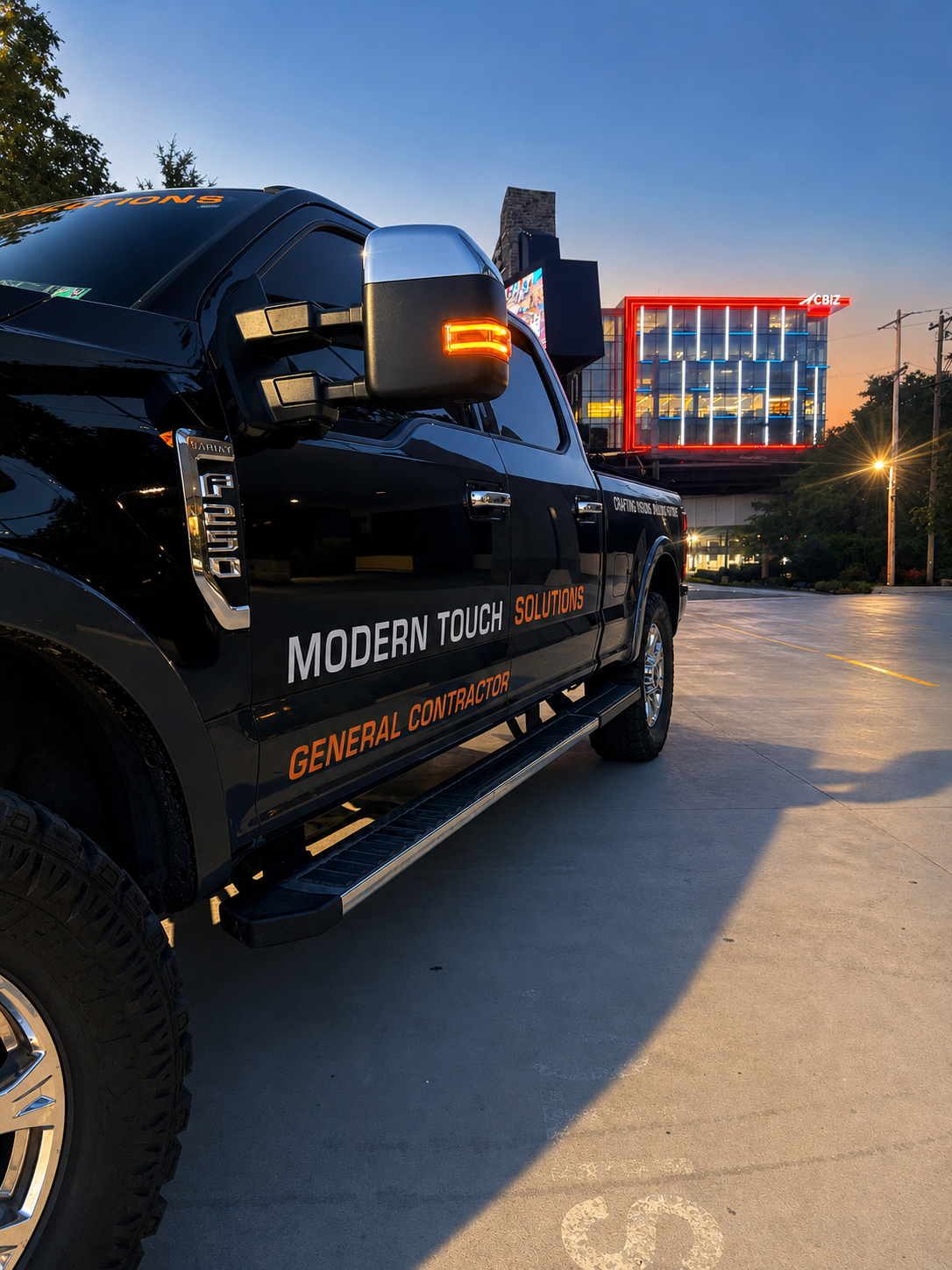 Black truck parked at dusk on a wet street, with a lit building in the background