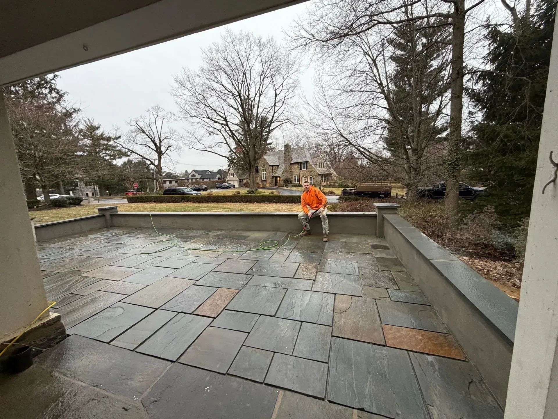 Person in an orange jacket working on a wet stone patio in a park-like outdoor area