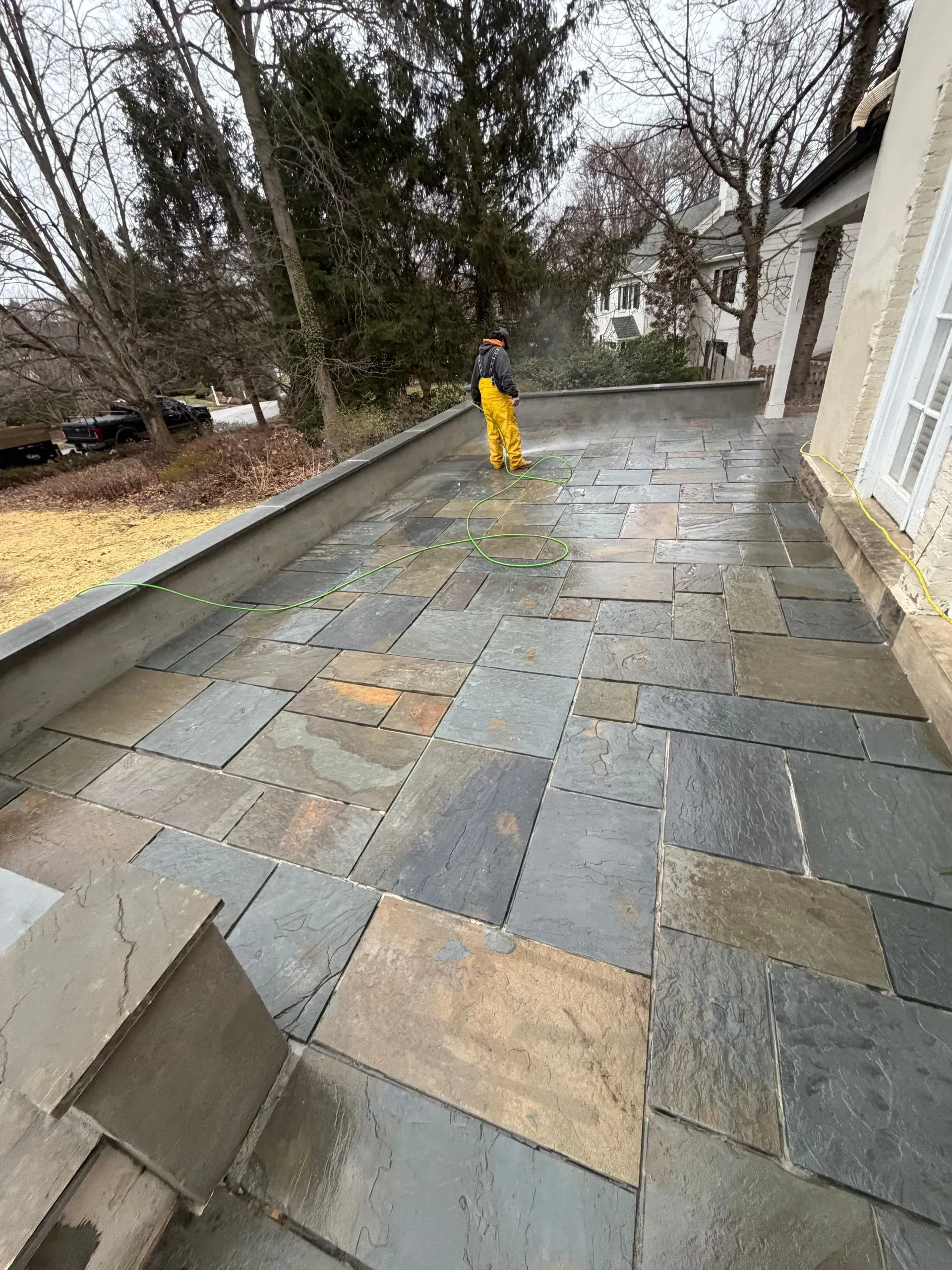 Rainy stone patio beside a house, with a yellow caution cone and bare trees nearby