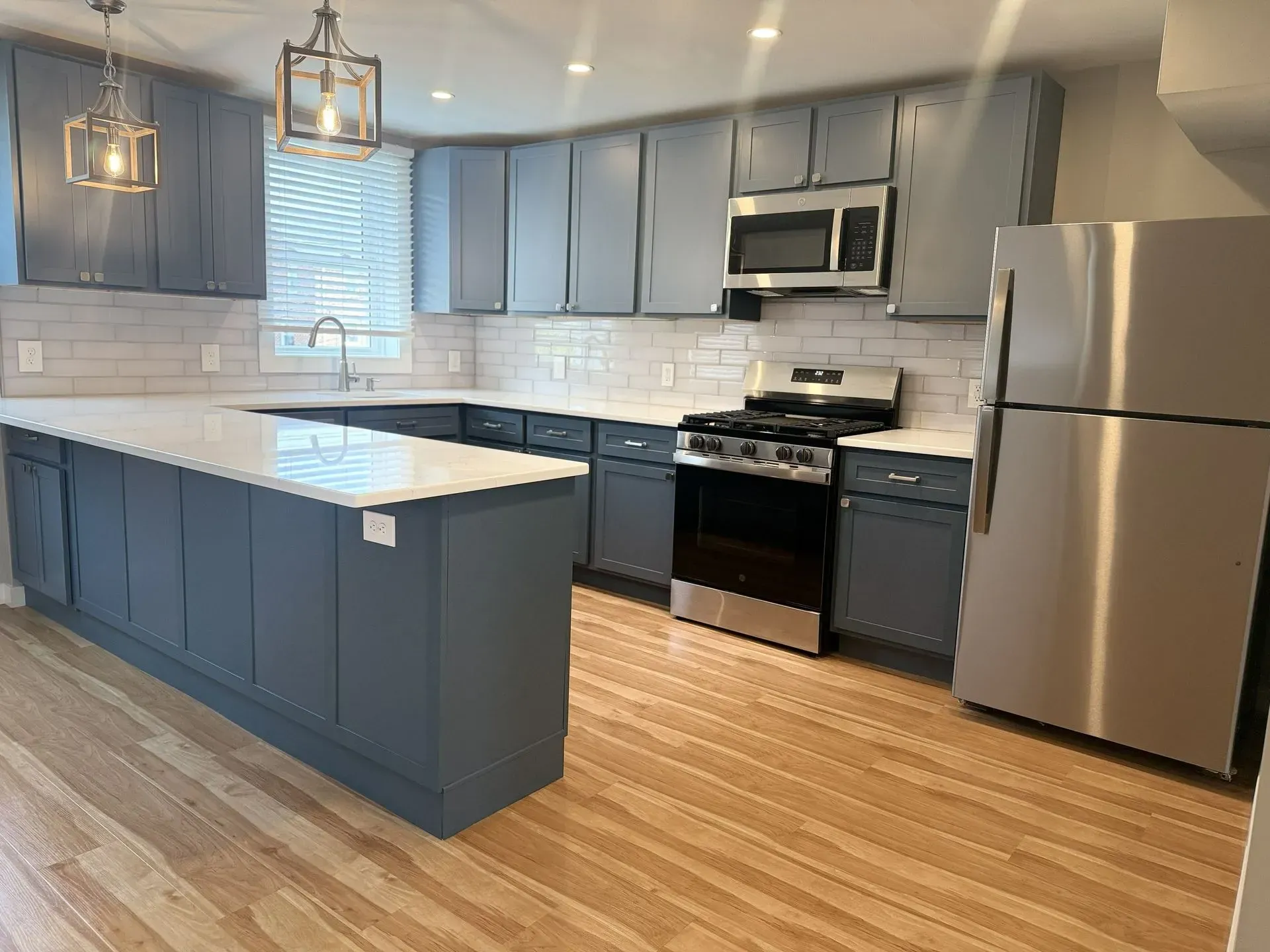 Modern kitchen with blue-gray cabinets, white island, stainless steel appliances, and wood floors.