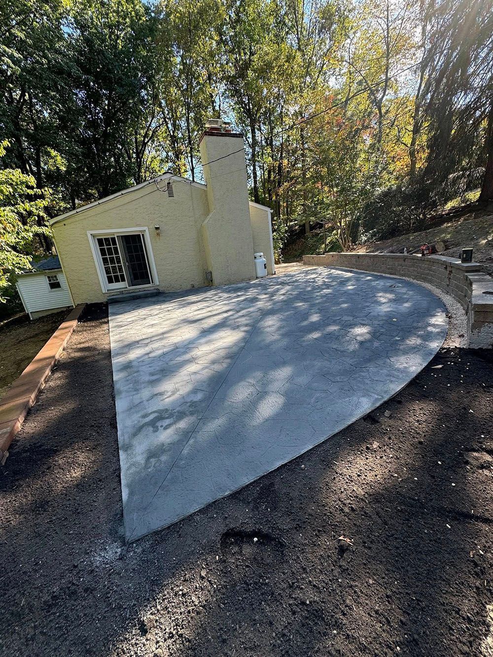 Small cream-colored building with a curved concrete patio in a wooded yard