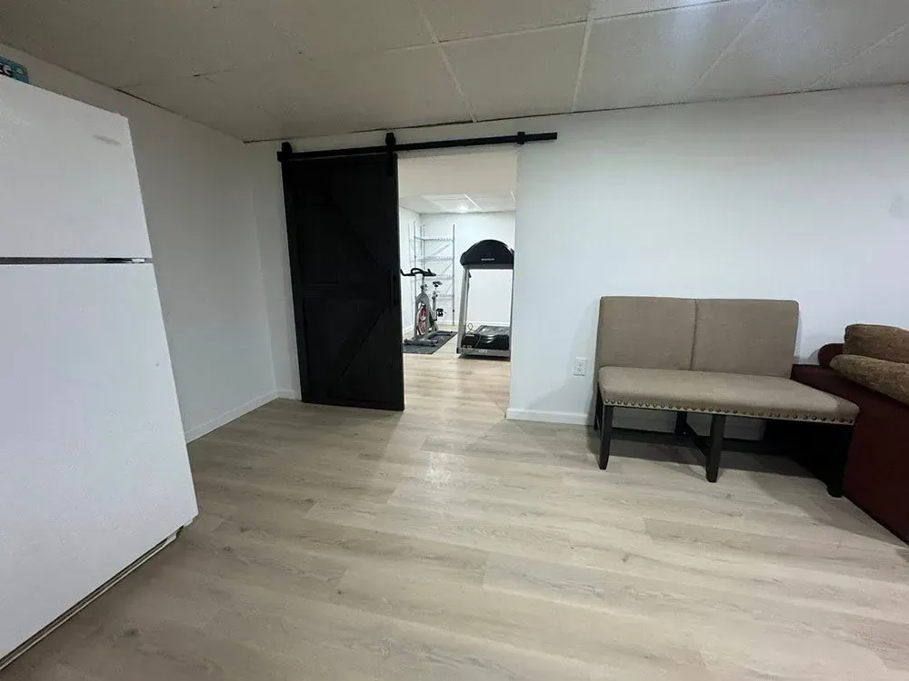 Small room with wood flooring, white fridge, black curtain doorway, and beige sofa bench.
