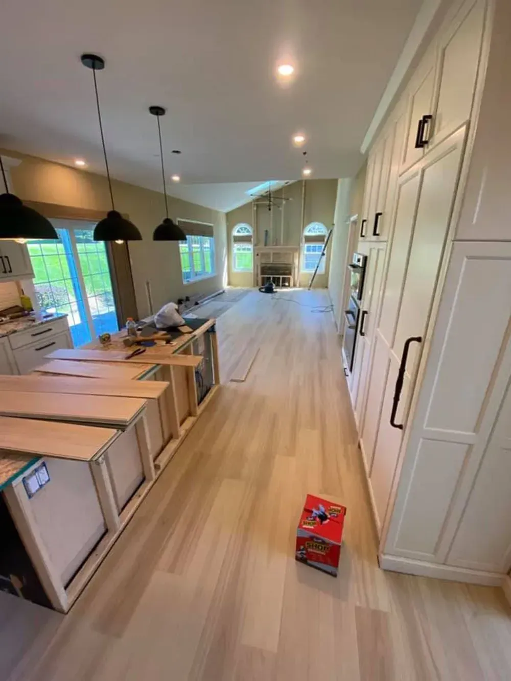 Modern kitchen with light wood floors, black pendant lights, and a long island leading to a bright dining area.