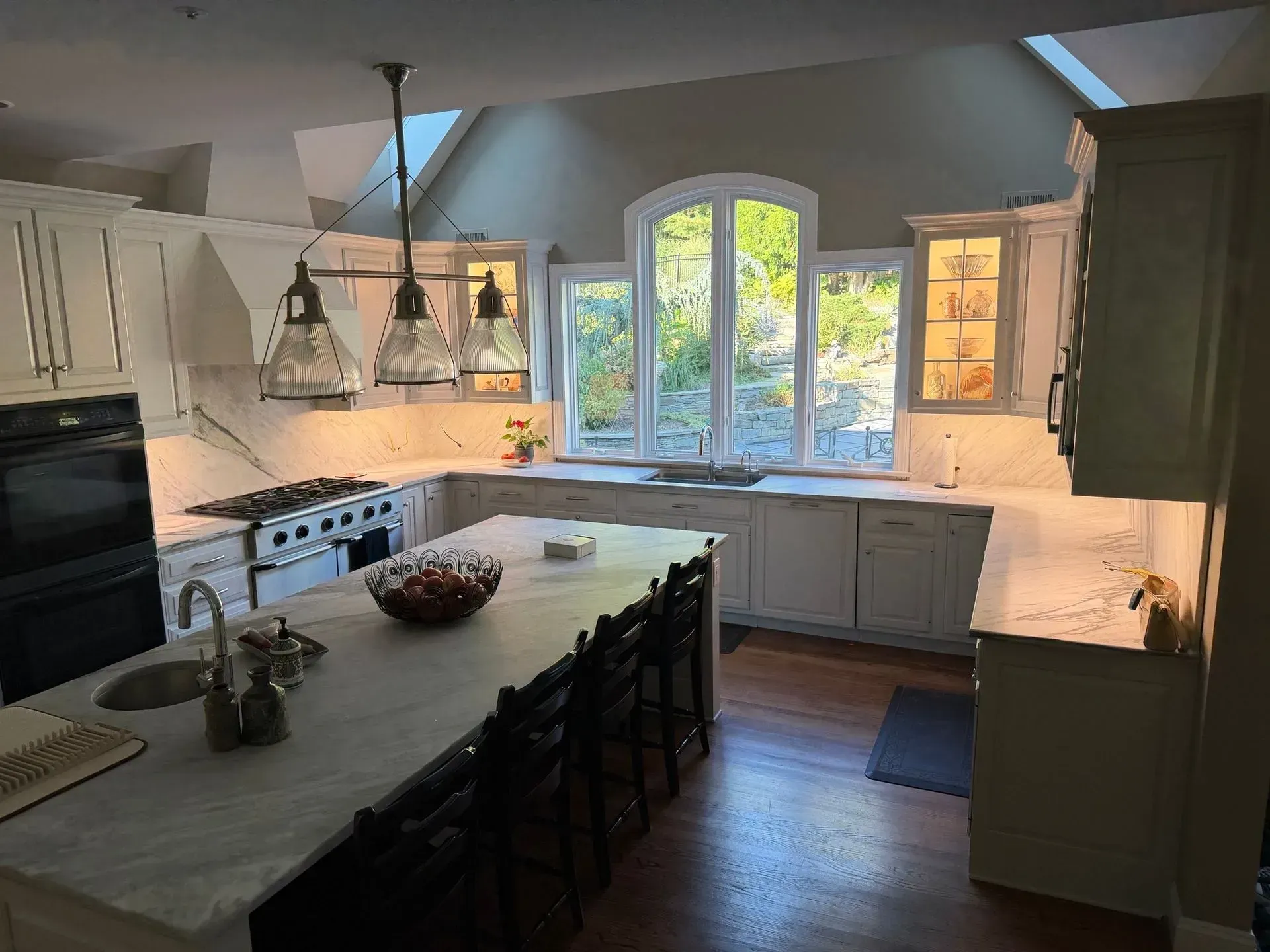 Bright kitchen with a central island, white cabinets, and a large window overlooking trees.