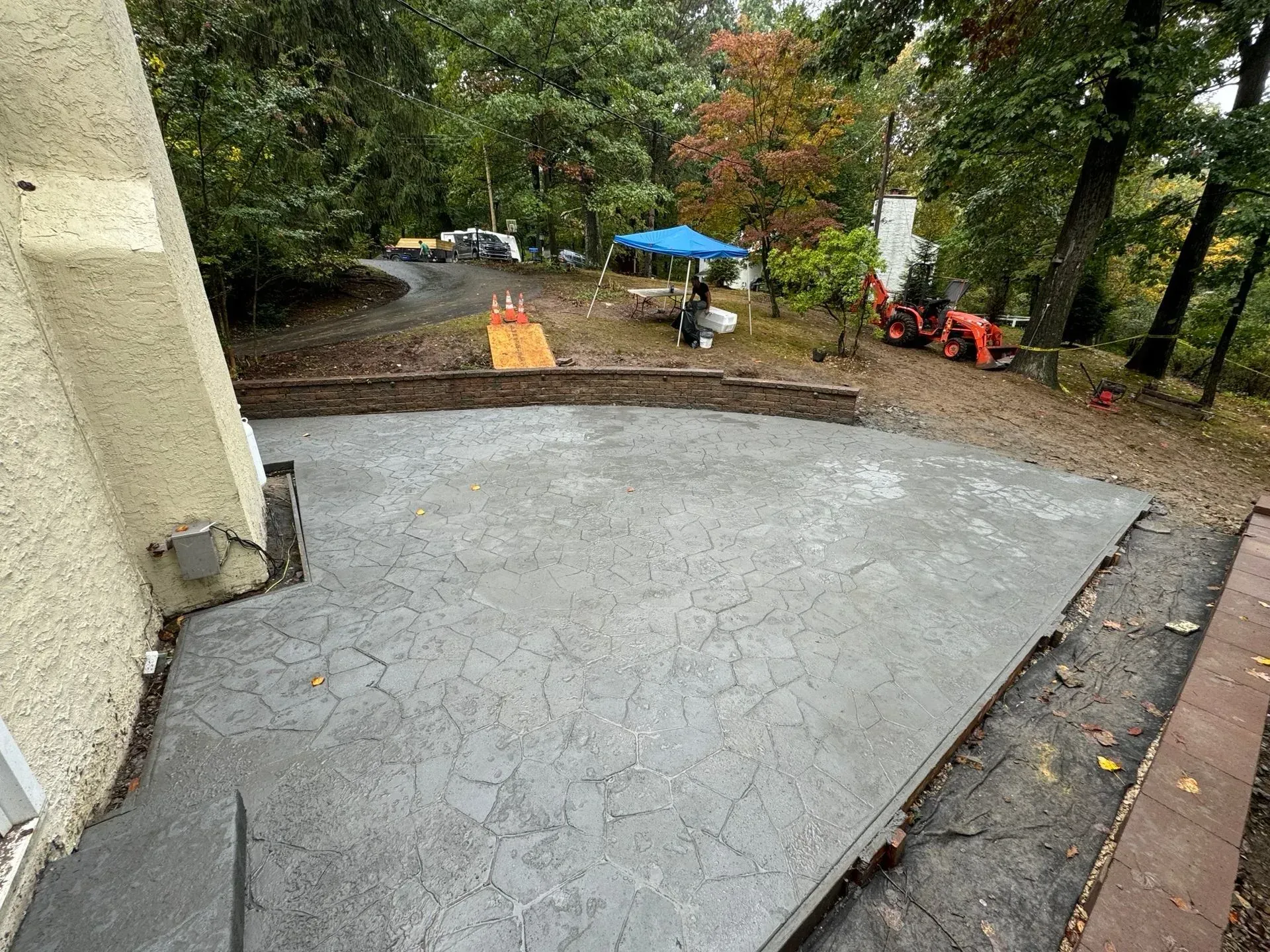 Freshly paved concrete driveway beside a house, with trees, a blue umbrella, and a small orange machine nearby