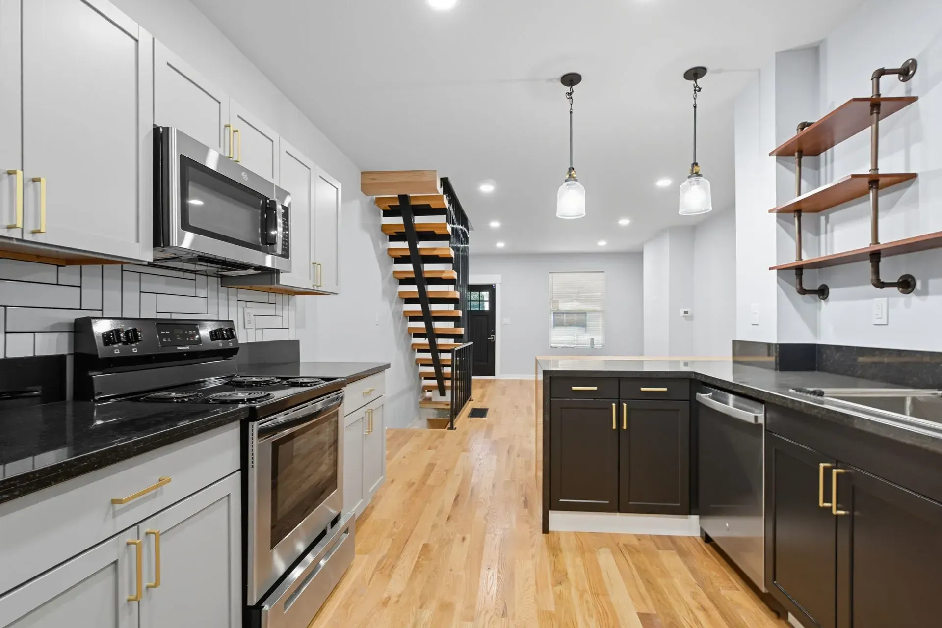 Modern white kitchen with stainless steel appliances, dark island cabinets, wood floors, and floating shelves