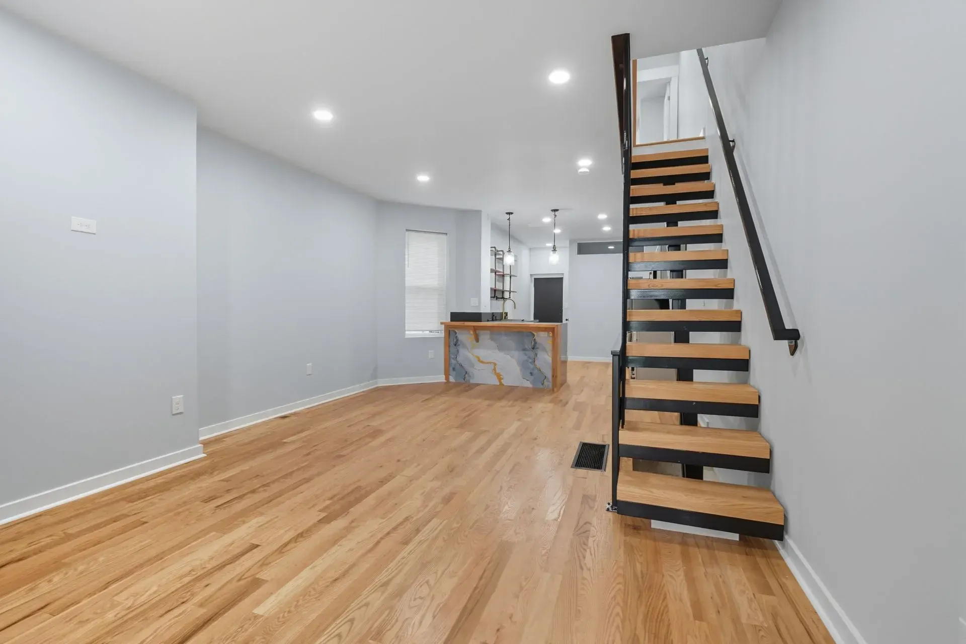 Empty modern living room with wood floors, gray walls, and a staircase leading upstairs.