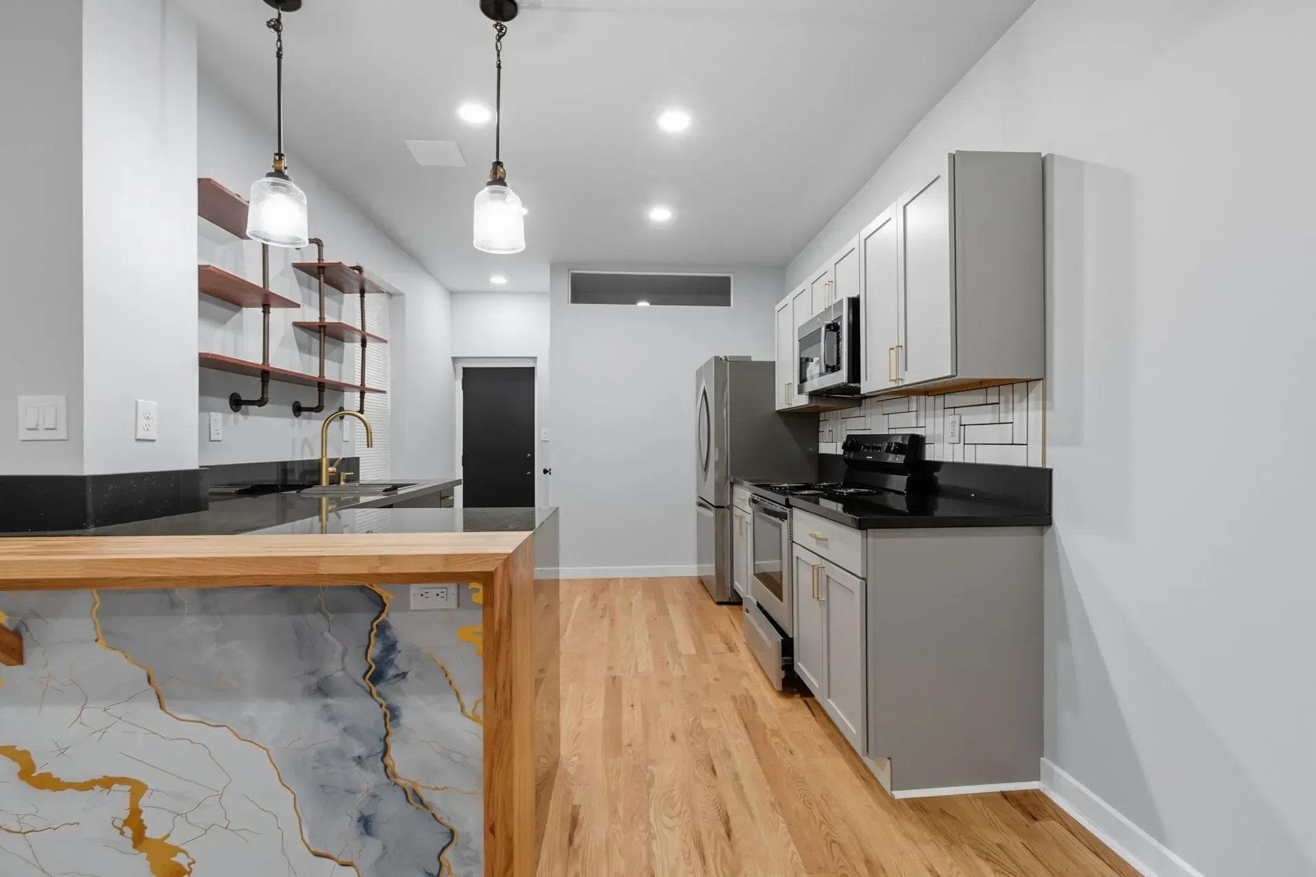 Modern kitchen with white cabinets, gray appliances, wood floor, and marble-topped island