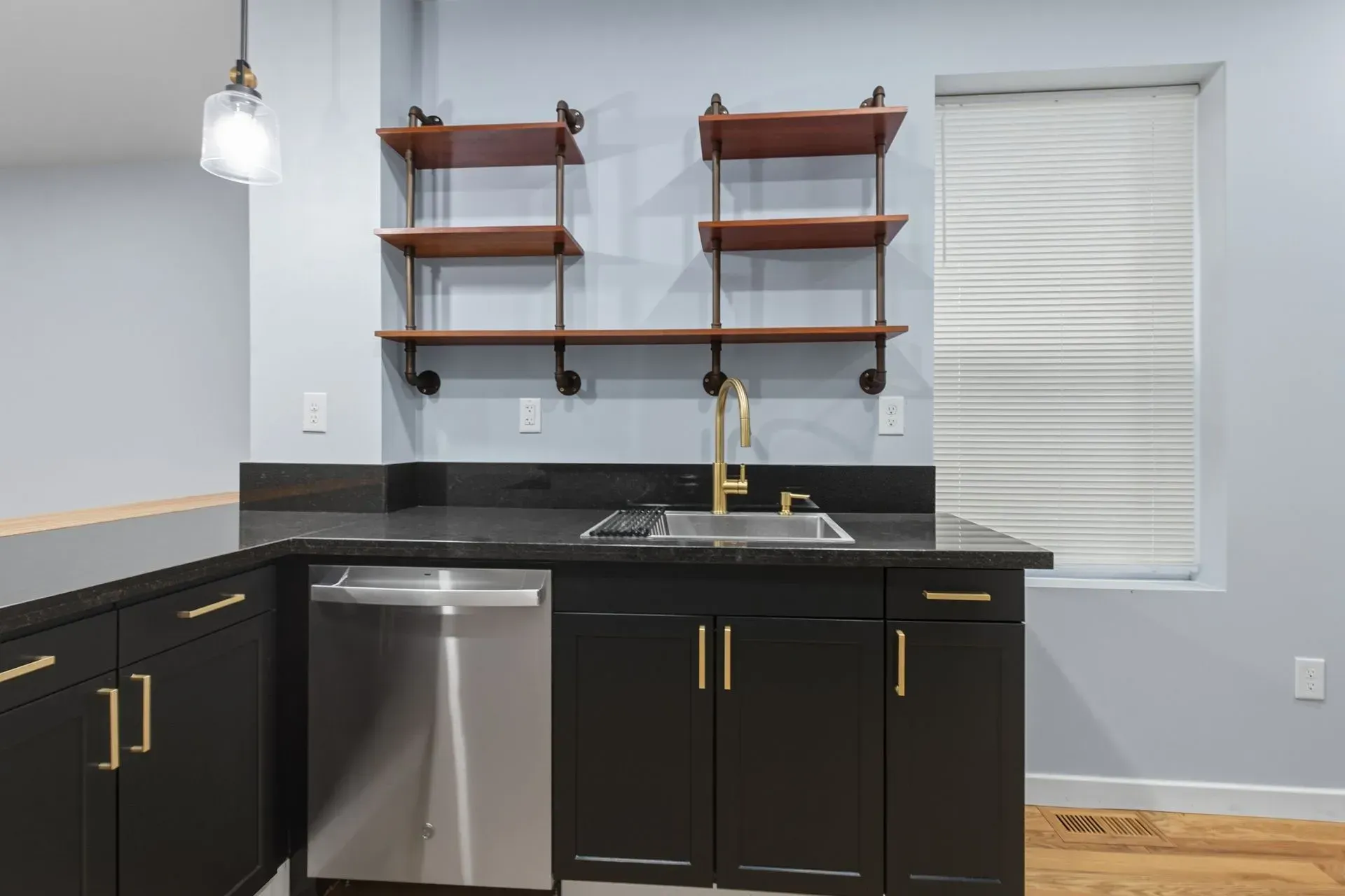 Modern kitchen with black cabinets, brass hardware, open wooden shelves, and a stainless-steel dishwasher