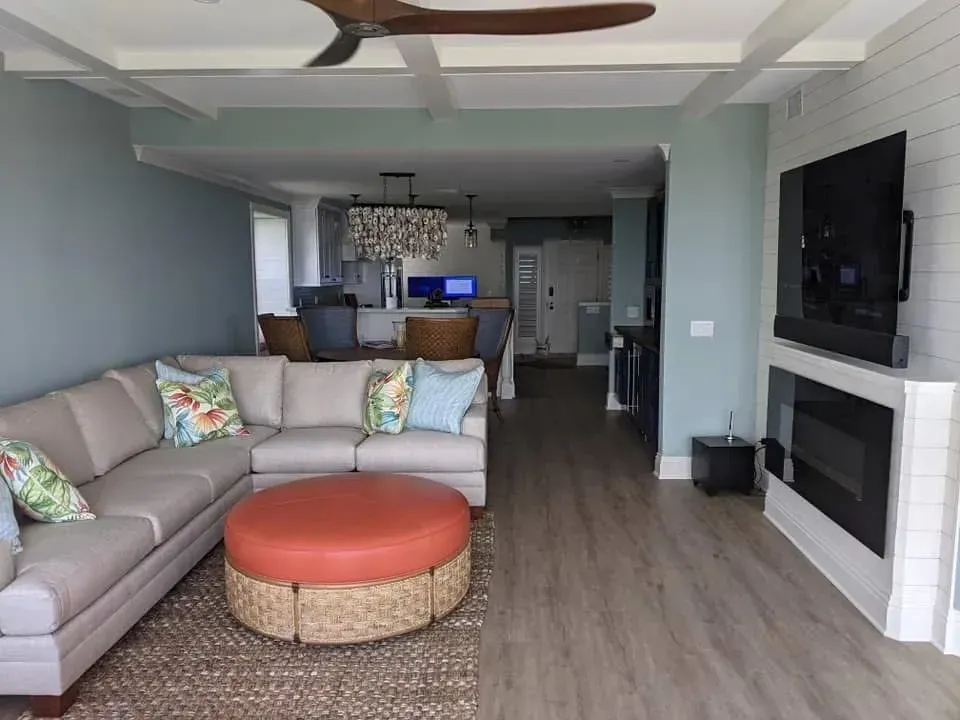 Living room with sectional sofa, orange ottoman, fireplace, and open floor plan.