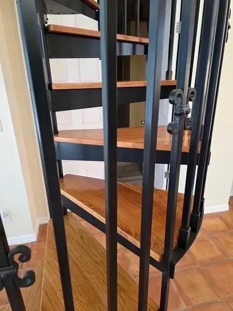 Black metal spiral staircase with wooden steps and railing.