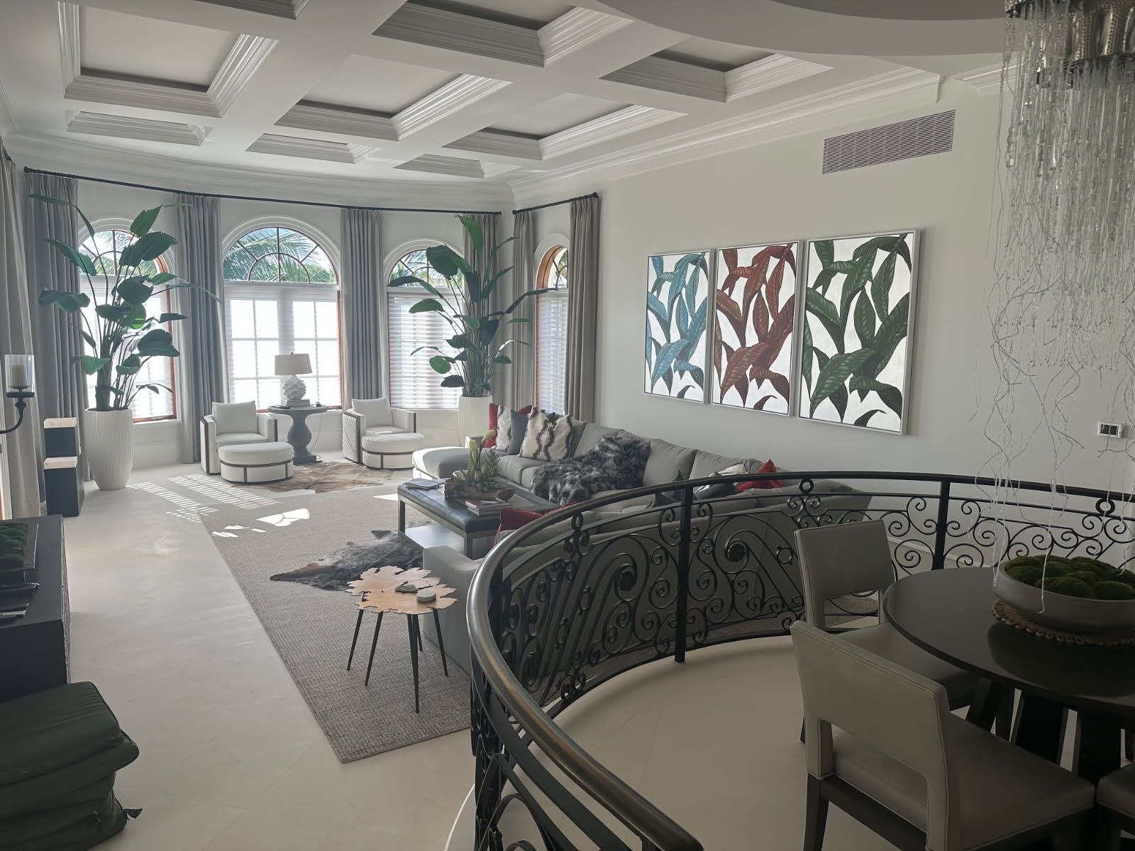 Elegant living room with large windows, artwork, and a balcony. White, gray, and brown tones are used throughout the space.