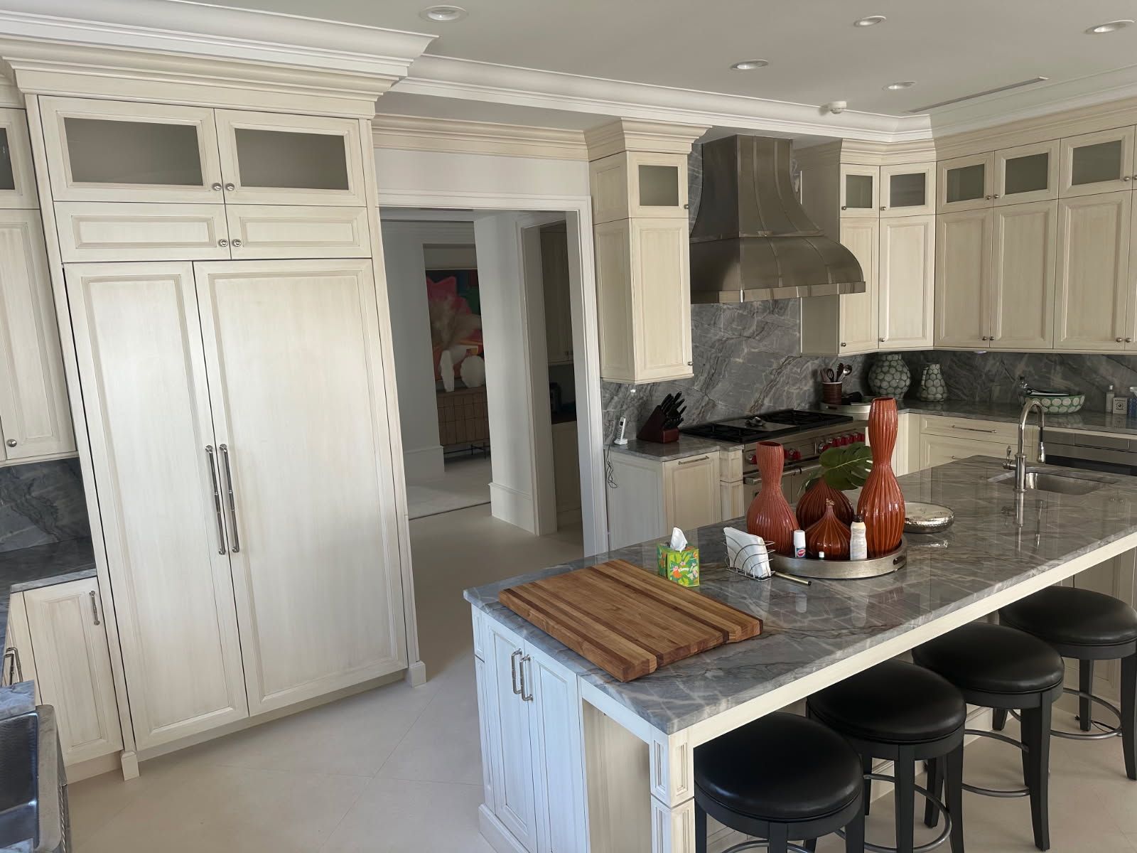 Kitchen with light cabinets, stainless steel appliances, marble countertop, and bar stools.