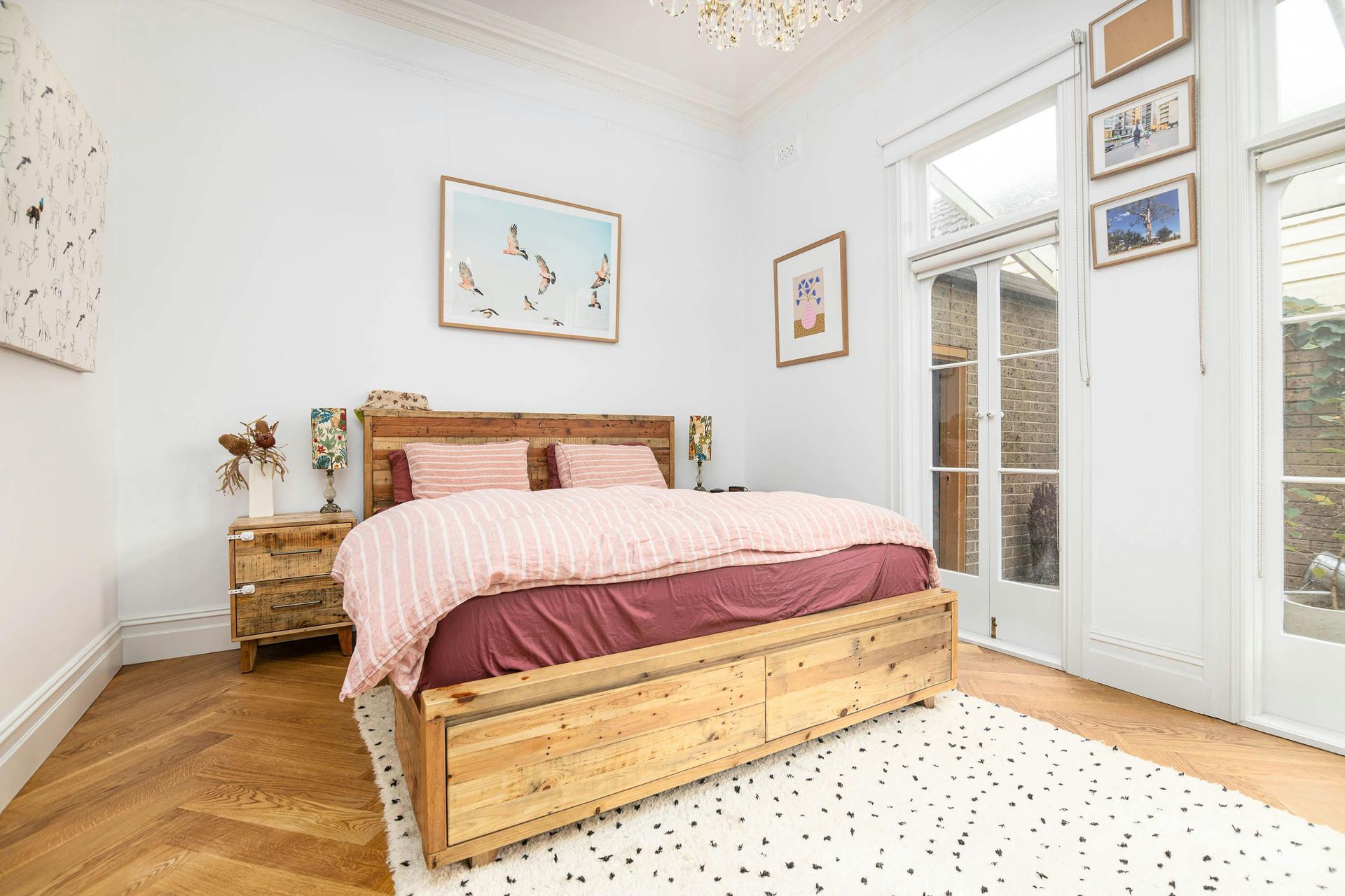 Bedroom with wooden bed frame, artwork, and French doors leading to a courtyard.